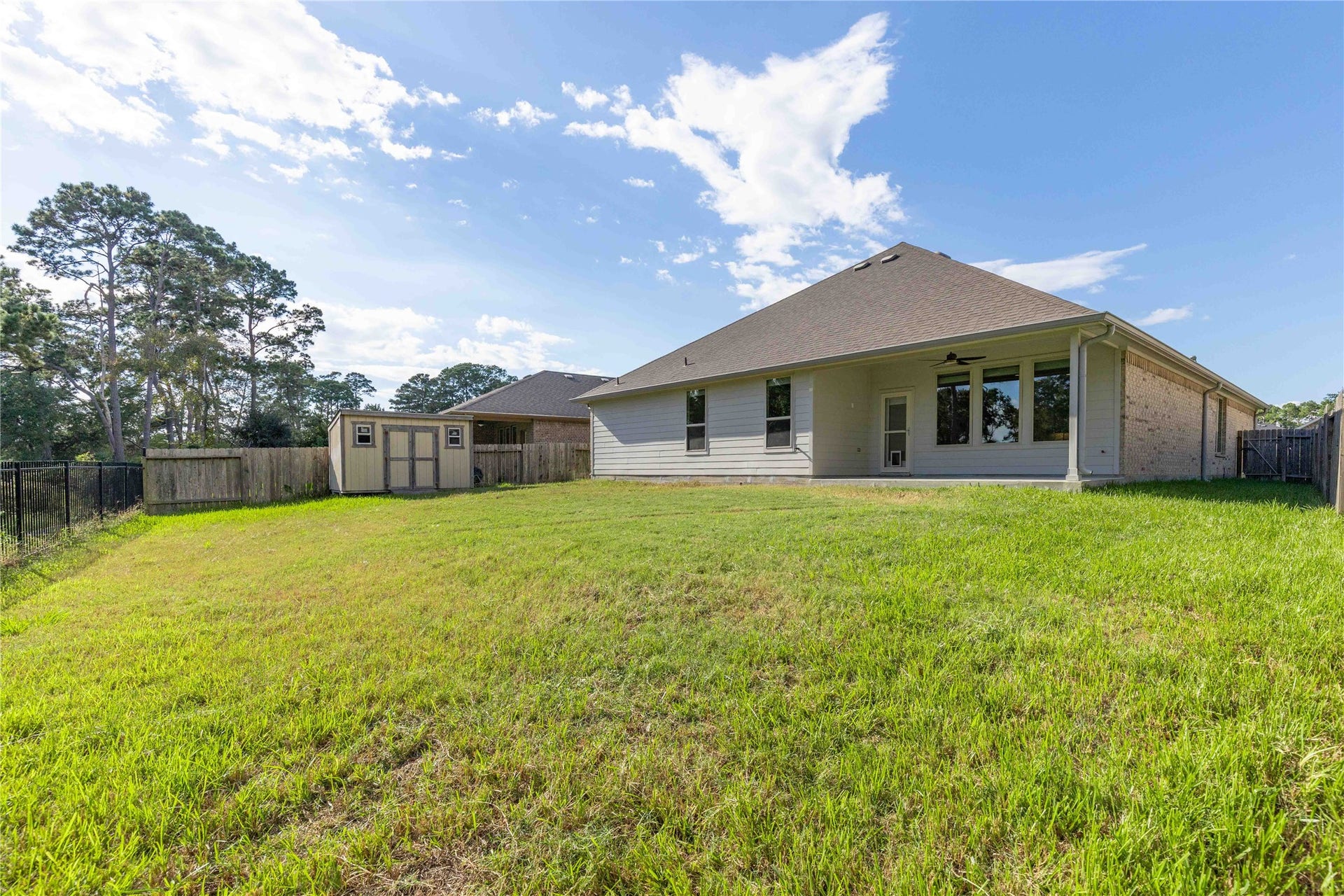 Spacious backyard with lush green lawn, a storage shed, and a covered patio, perfect for outdoor activities and relaxation.
