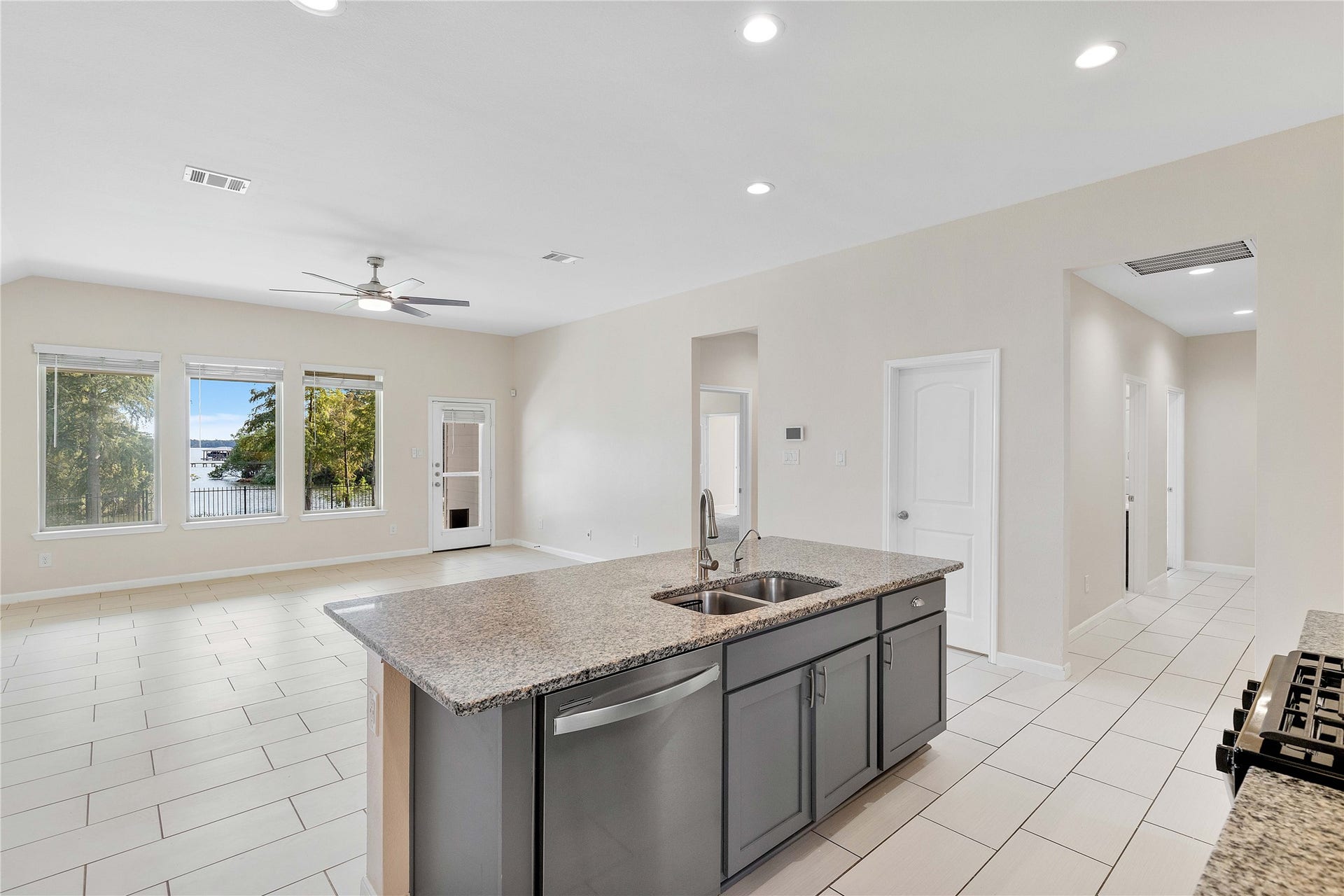 Bright and spacious open-concept living area featuring a modern kitchen with a large granite island, stainless steel appliances, and tile flooring, complemented by large windows offering scenic views.