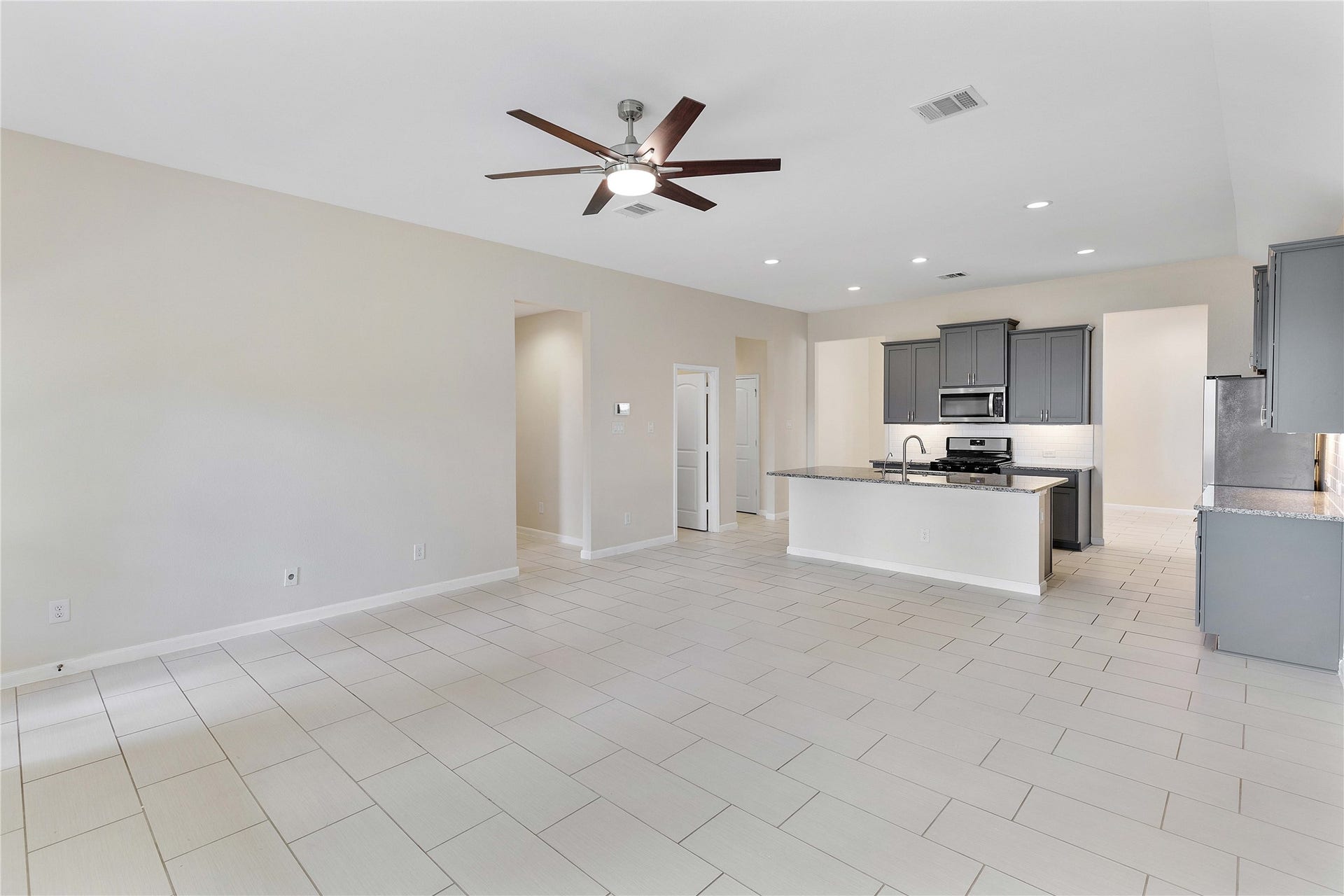 Spacious open-concept living area with sleek tile flooring, modern ceiling fan, and a stylish kitchen featuring granite countertops and stainless steel appliances.