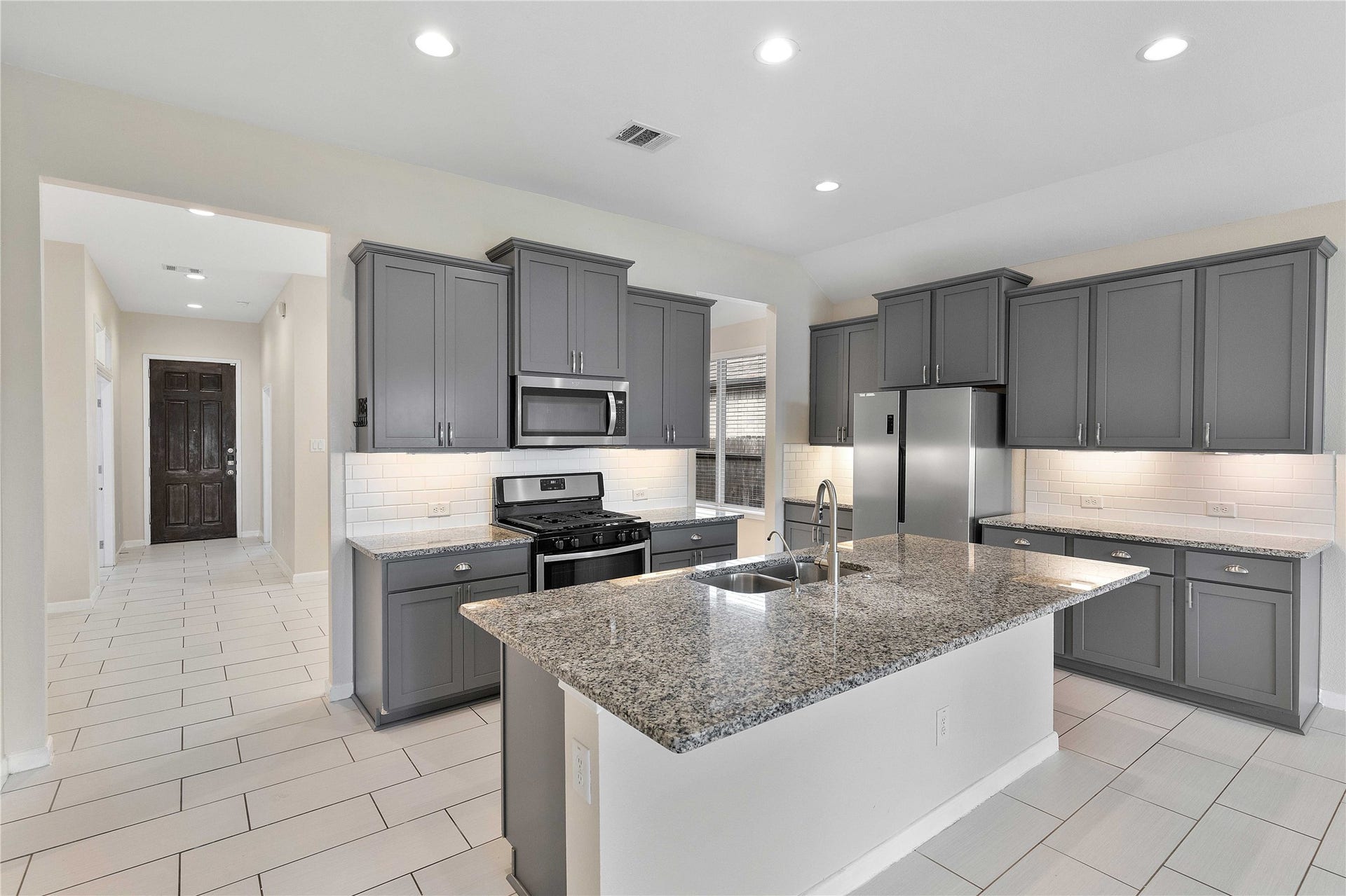 Modern kitchen featuring granite countertops, sleek gray cabinetry, stainless steel appliances, and a central island with ample workspace.