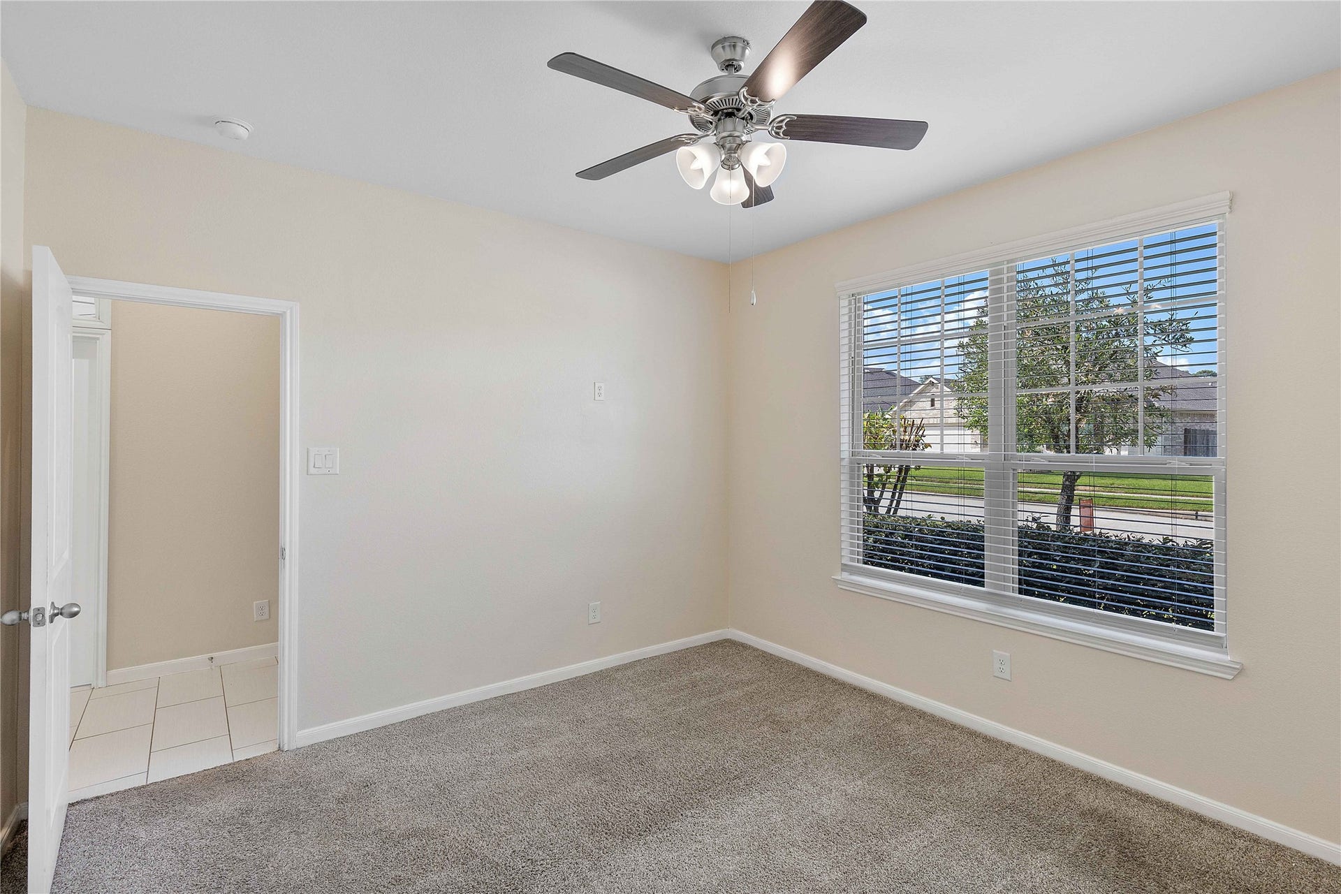 Bright and inviting room featuring plush carpeting, a ceiling fan, and a large window offering plenty of natural light.