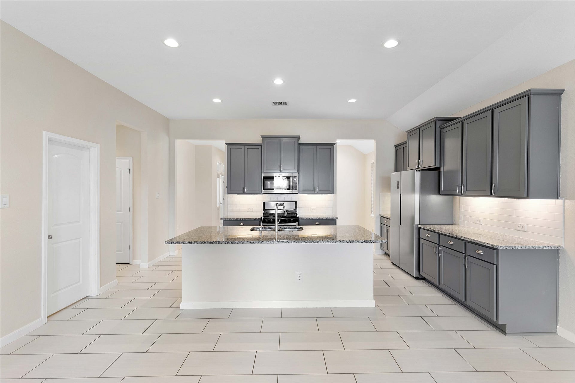 Modern kitchen with sleek gray cabinetry, granite countertops, and stainless steel appliances, offering ample space and contemporary style.