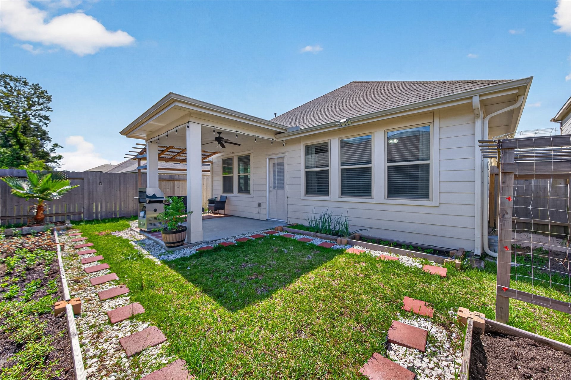 22409 Kinley Street, New Caney, TX 77357 A charming backyard with a covered patio, perfect for relaxation or entertaining. The space features a small garden area with a tidy lawn and a pathway lined with decorative stones.