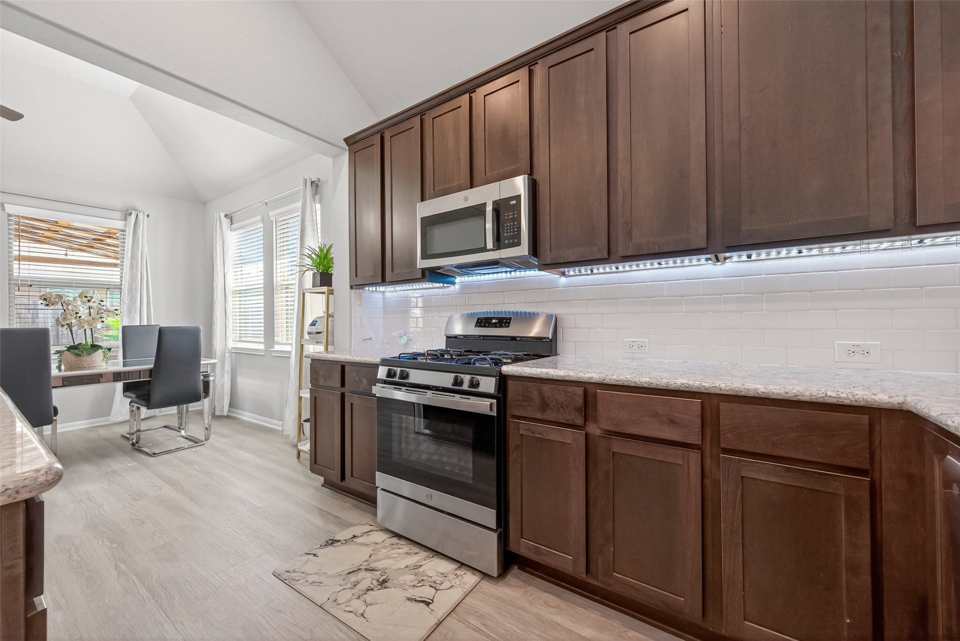 22409 Kinley Street, New Caney, TX 77357 This kitchen features modern stainless steel appliances, dark wood cabinetry, and granite countertops. It opens to a bright dining area with large windows and a view of the outside patio.