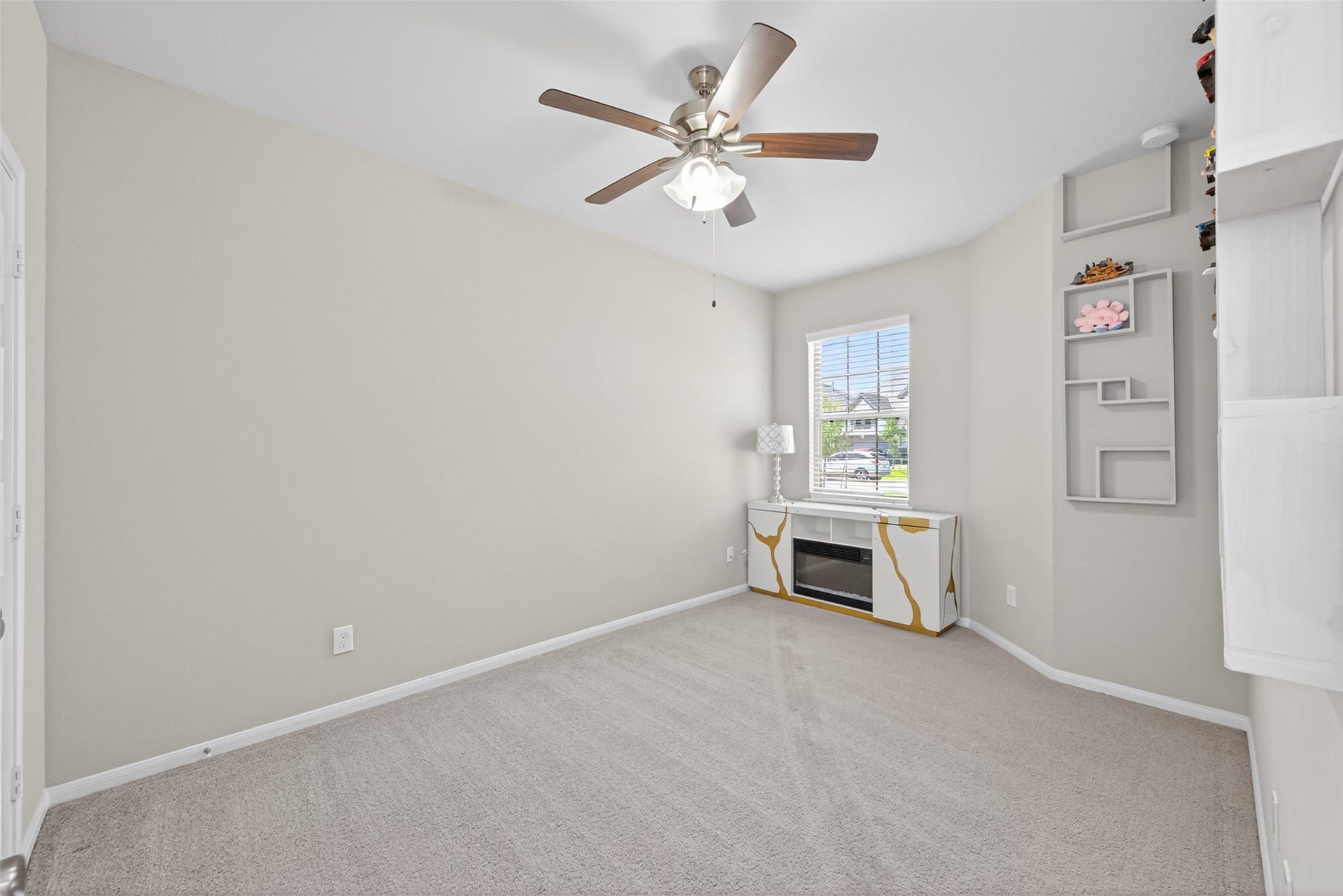 22409 Kinley Street, New Caney, TX 77357 This room features neutral walls and carpet, a ceiling fan, and ample natural light from a window. Built-in shelves and a small entertainment unit provide extra storage and display options. Could serve as an office or another bedroom.
