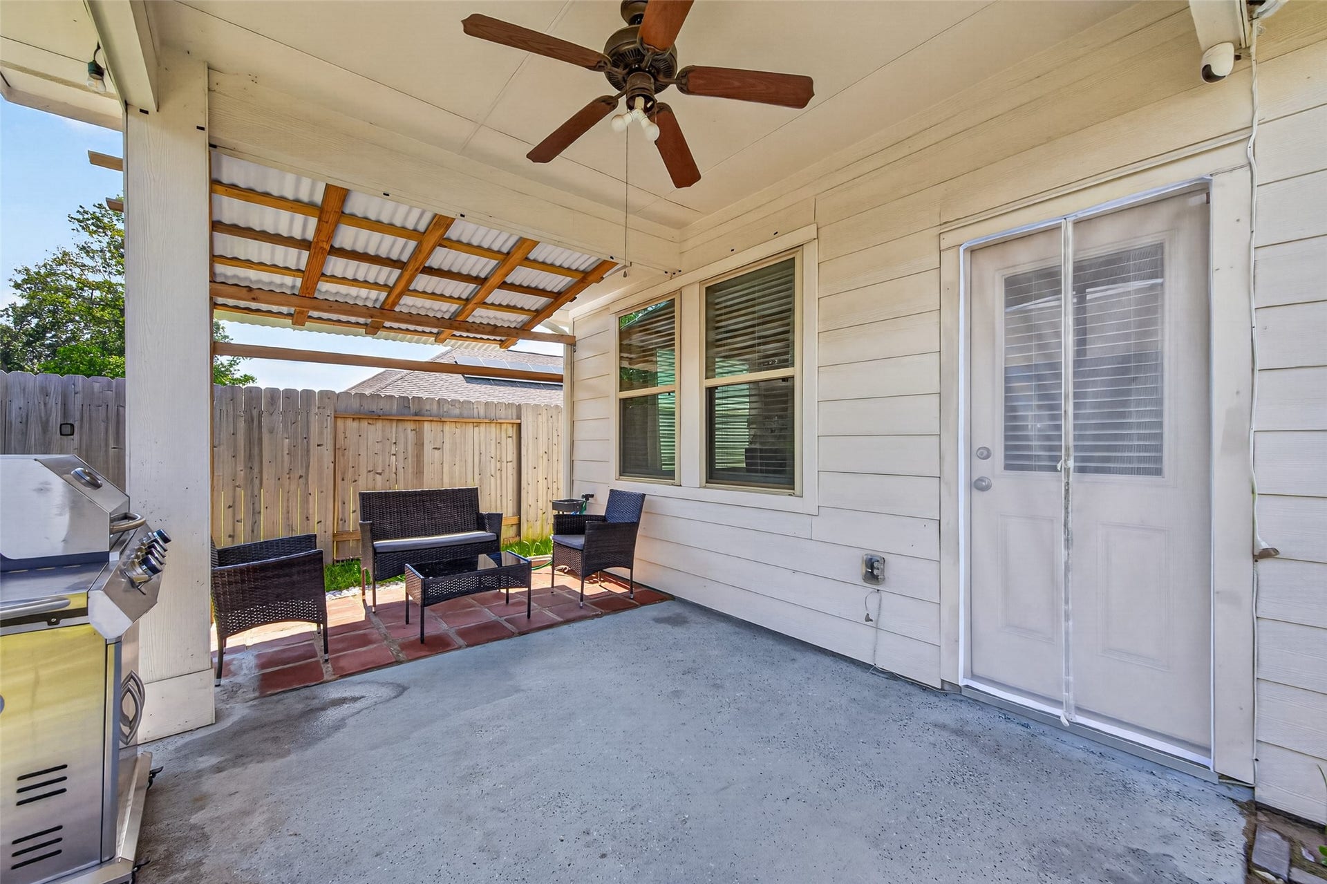 22409 Kinley Street, New Caney, TX 77357 A cozy covered patio with a ceiling fan, outdoor seating, and a grill, perfect for relaxing or entertaining. The space is enclosed by a wooden fence, providing privacy.