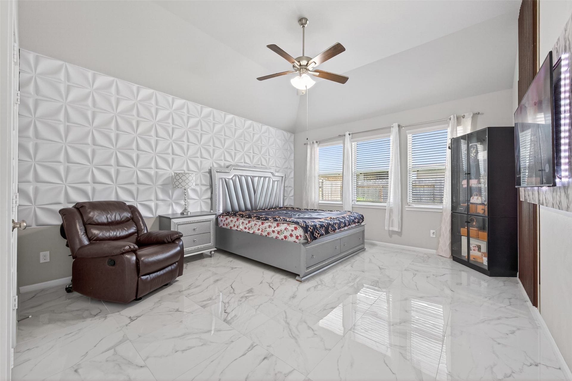 22409 Kinley Street, New Caney, TX 77357 This spacious primary bedroom features a modern design with a unique textured accent wall, large windows for natural light, glossy marble-like flooring.