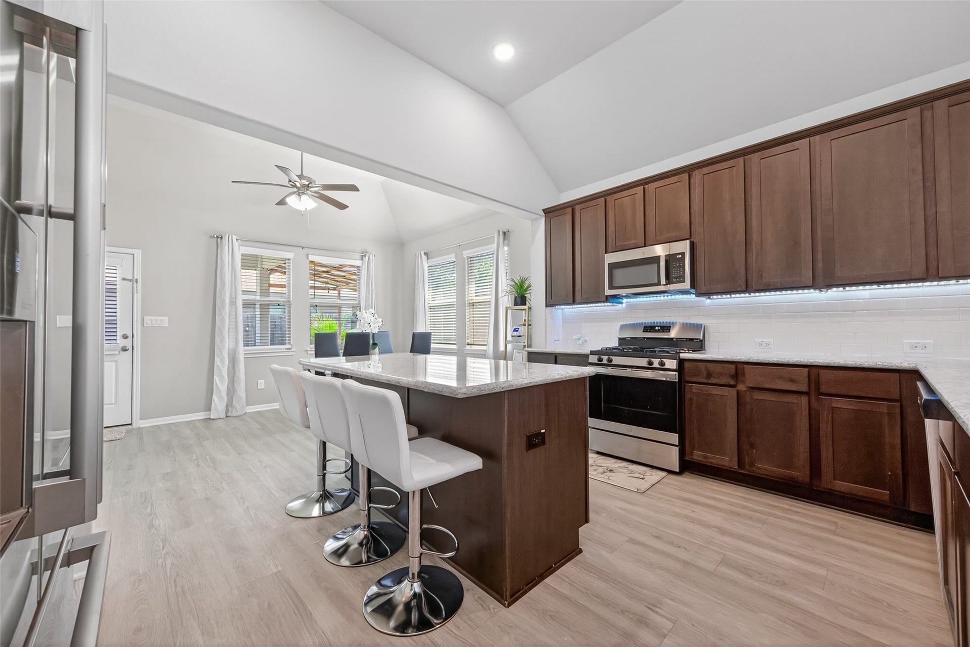 22409 Kinley Street, New Caney, TX 77357 This modern kitchen features high ceilings, sleek stainless steel appliances, and ample natural light. It includes an island with seating, dark wood cabinetry, and stylish lighting, creating a welcoming and functional space.