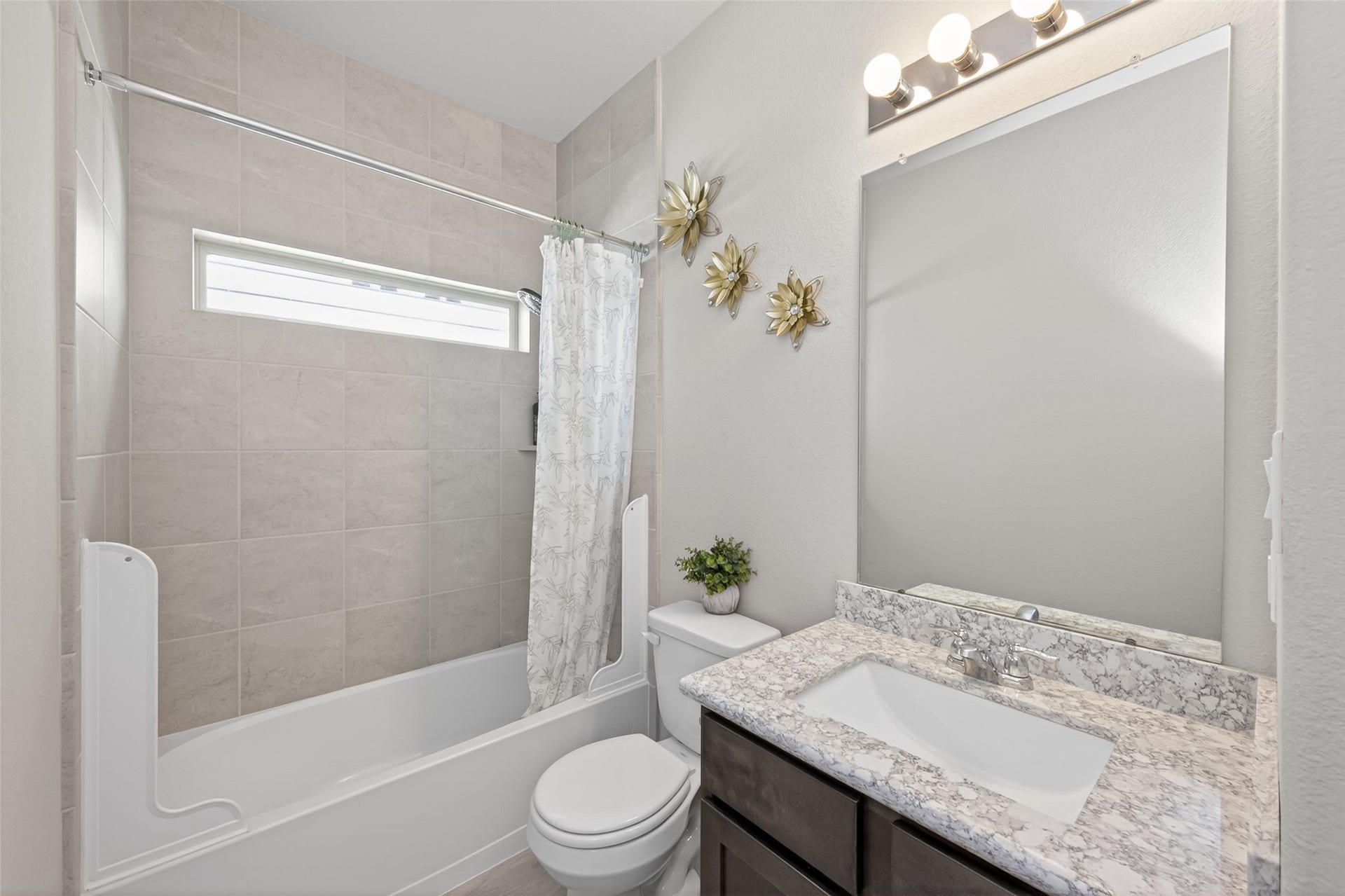 22409 Kinley Street, New Caney, TX 77357 This secondary bathroom features a modern design with a granite countertop, a large mirror with overhead lighting, and a tiled shower-tub combo.