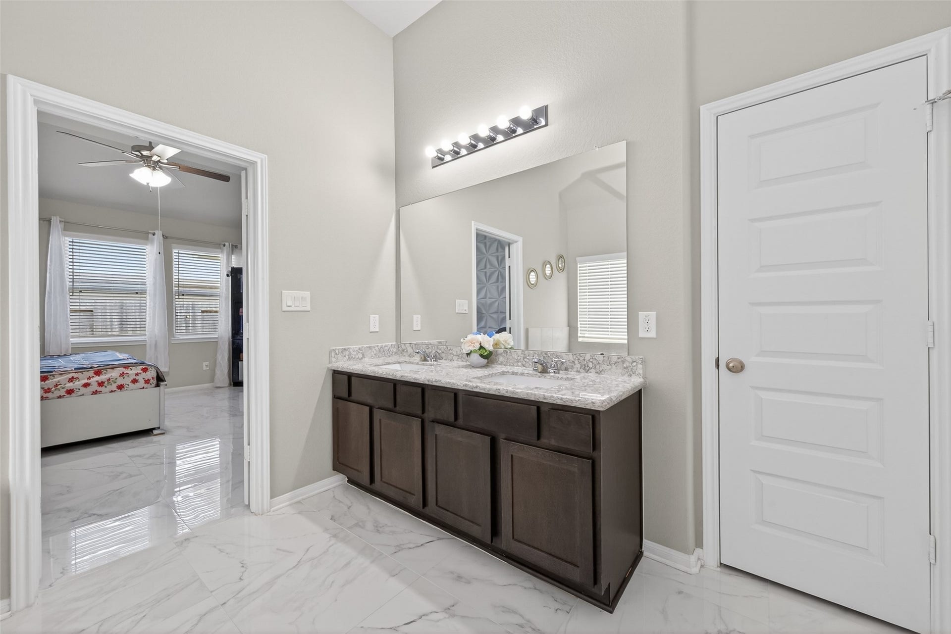 22409 Kinley Street, New Caney, TX 77357 A modern bathroom with a sleek vanity featuring a large mirror and granite countertop. The space connects to a bedroom with marble-style flooring.