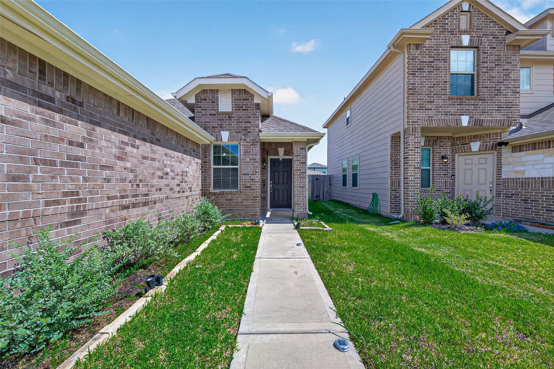 22409 Kinley Street, New Caney, TX 77357 A welcoming front walkway, flanked by well-maintained greenery. It's nestled between neighboring houses, offering a cozy and inviting entrance.