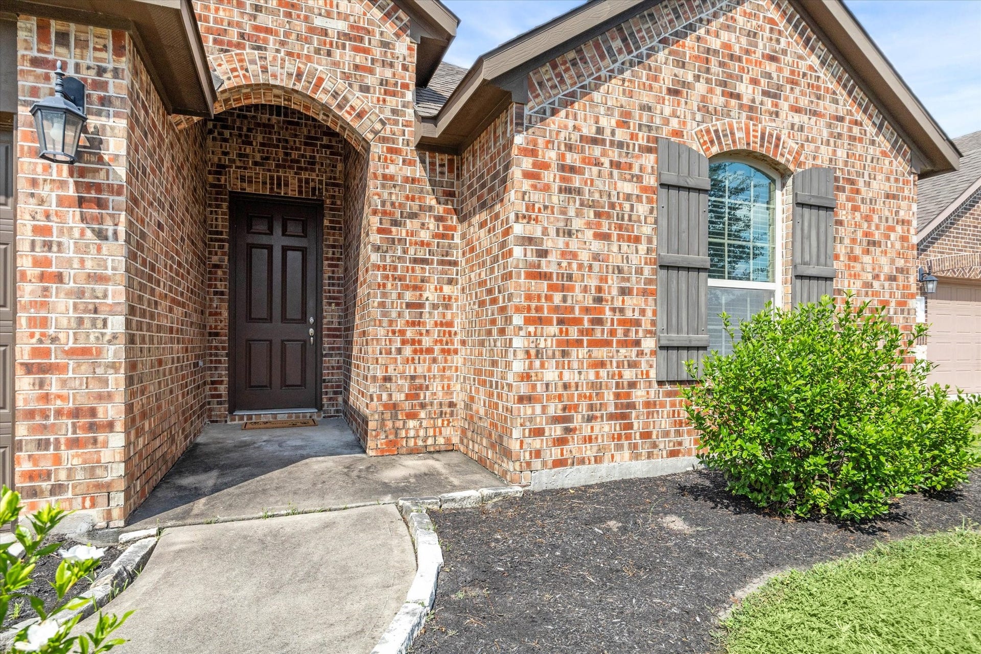 6610 Auburn Terrace Lane, Rosenberg, TX 77471 Charming brick home featuring a welcoming arched entryway, a decorative front door, and a quaint window with shutters, set in a well-maintained landscape.