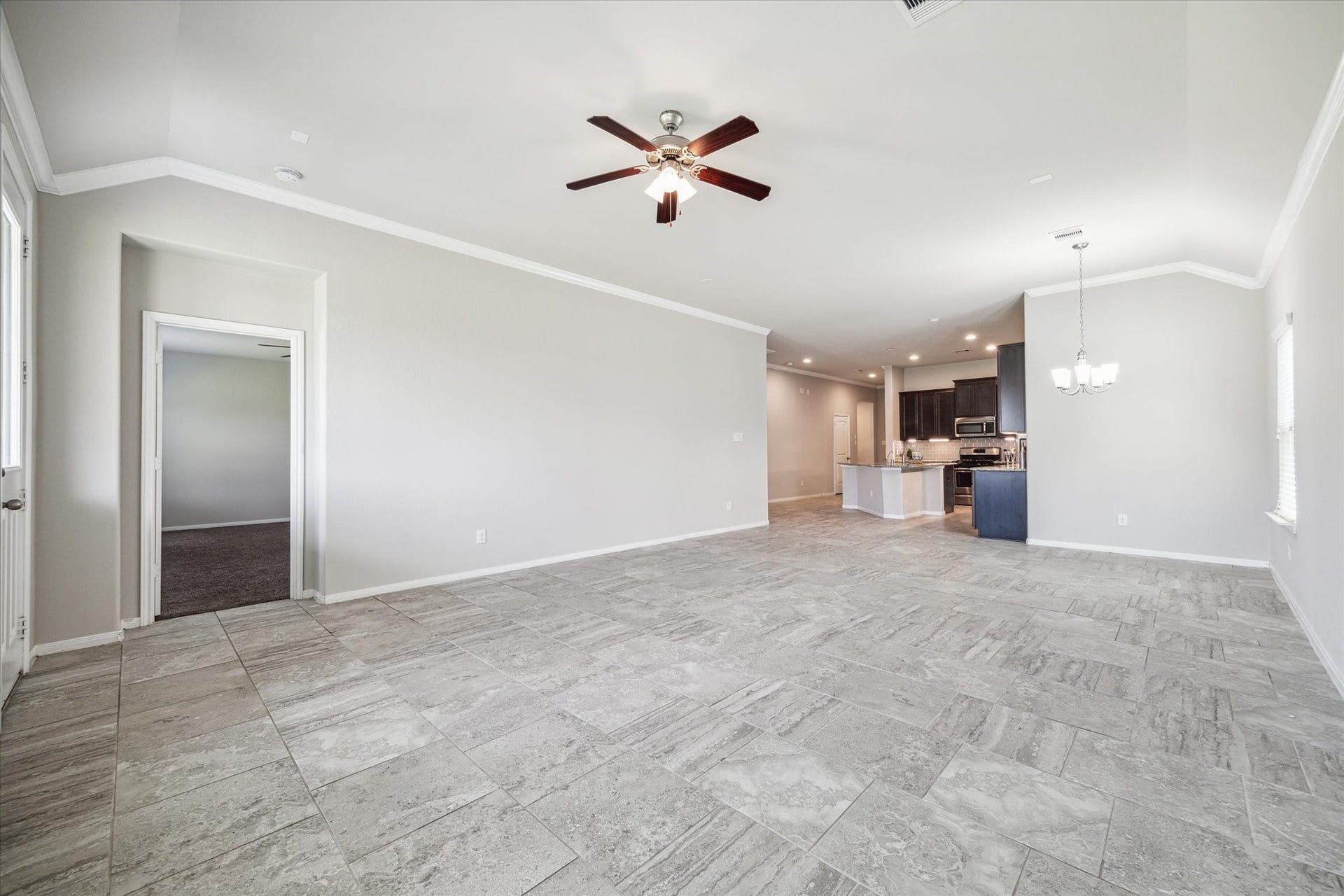 6610 Auburn Terrace Lane, Rosenberg, TX 77471 This is a spacious, open-concept living area with tile flooring, featuring a living room and an adjoining kitchen with modern appliances. It has ample natural light, a ceiling fan, and a neutral color palette.