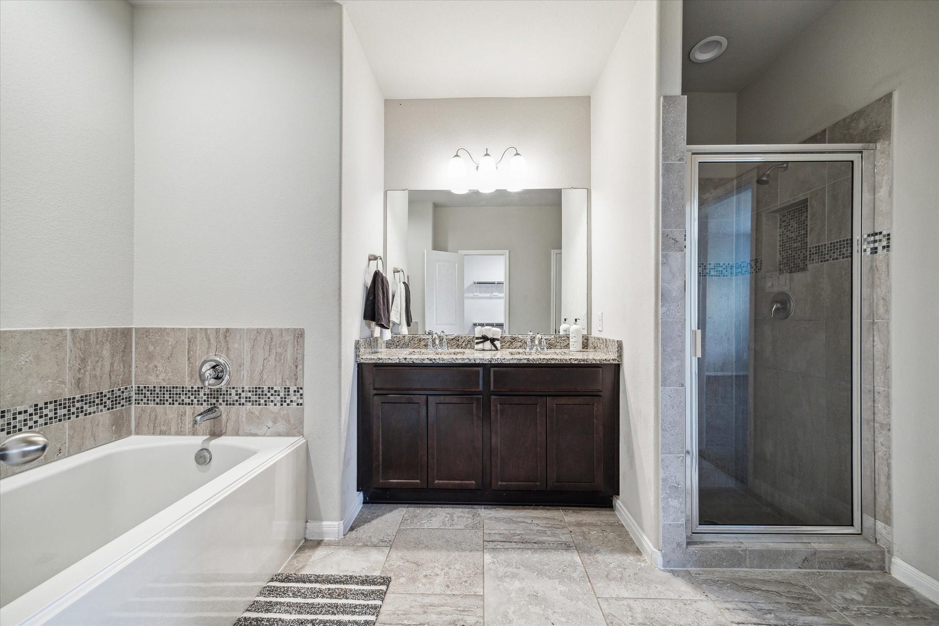 6610 Auburn Terrace Lane, Rosenberg, TX 77471 This is a modern, spacious bathroom featuring a large soaking tub, a glass-enclosed shower, a dual-sink vanity with ample storage, and elegant tile work throughout.