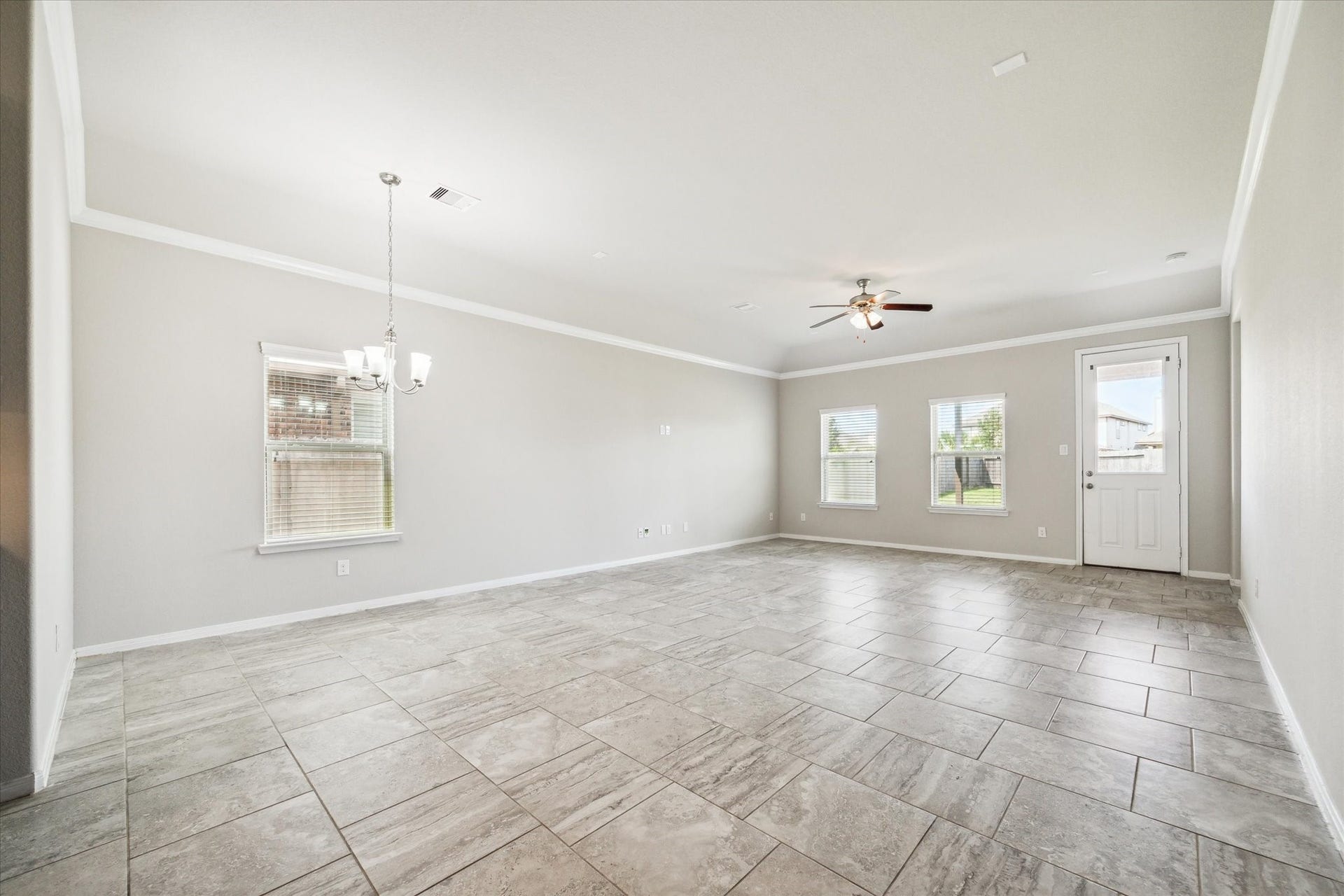 6610 Auburn Terrace Lane, Rosenberg, TX 77471 This is a spacious, well-lit room with modern tile flooring, neutral wall colors, recessed lighting, a ceiling fan, and multiple windows providing natural light. It appears to be move-in ready.