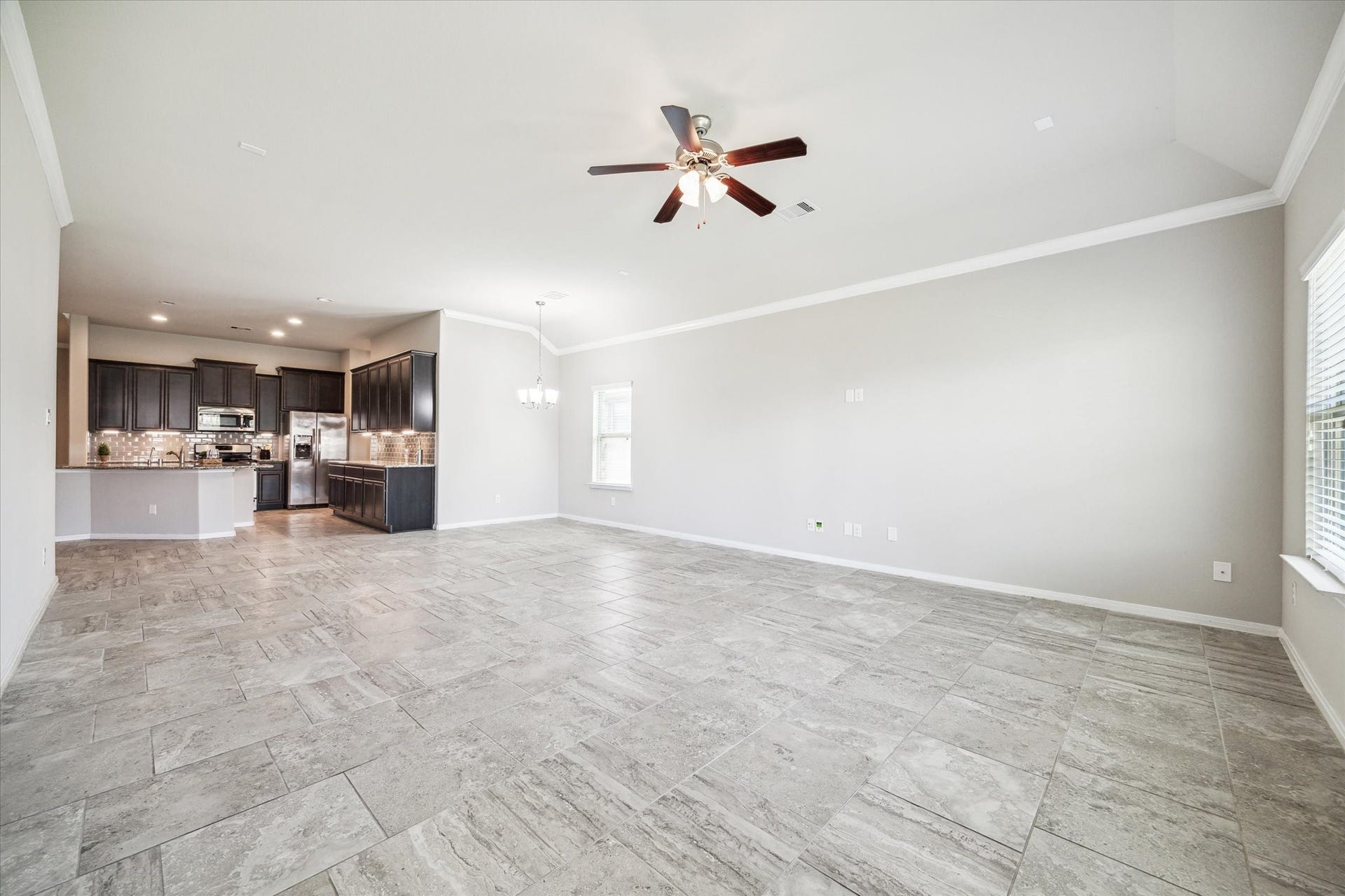 6610 Auburn Terrace Lane, Rosenberg, TX 77471 This is a spacious, open-concept living space with a modern kitchen featuring dark cabinetry and stainless steel appliances. The room has large tiled flooring, ample natural light, and a ceiling fan for comfort.