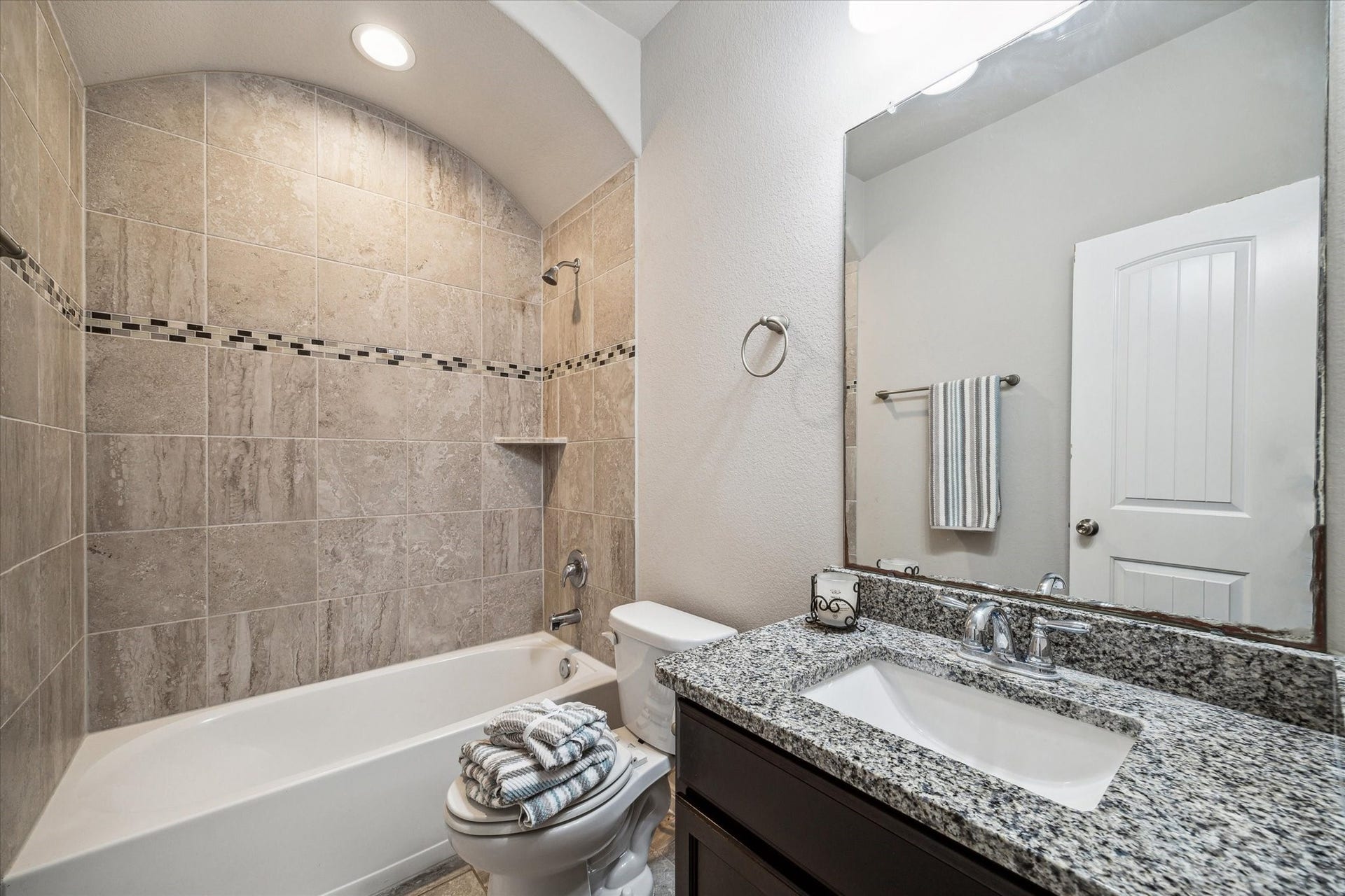 6610 Auburn Terrace Lane, Rosenberg, TX 77471 This is a modern bathroom featuring a tiled bathtub with a shower, a granite countertop with a single sink, and a large mirror, complemented by good lighting and neutral tones.