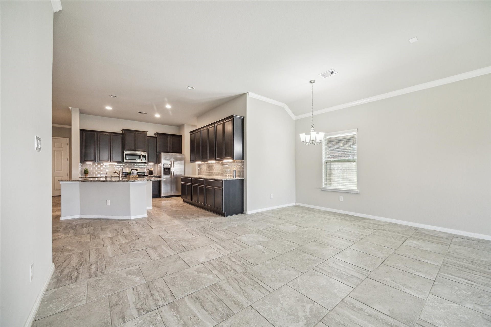 6610 Auburn Terrace Lane, Rosenberg, TX 77471 This photo features a spacious, open-concept living area with a modern kitchen showcasing dark cabinets and stainless steel appliances. The room benefits from ample natural light and is finished with large, tiled flooring.