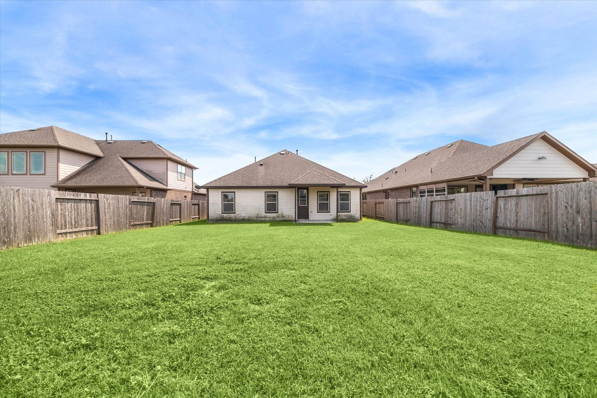 6610 Auburn Terrace Lane, Rosenberg, TX 77471 Spacious backyard with lush green lawn, enclosed by a privacy fence with a view of the rear side of a single-story home featuring large windows and a patio.
