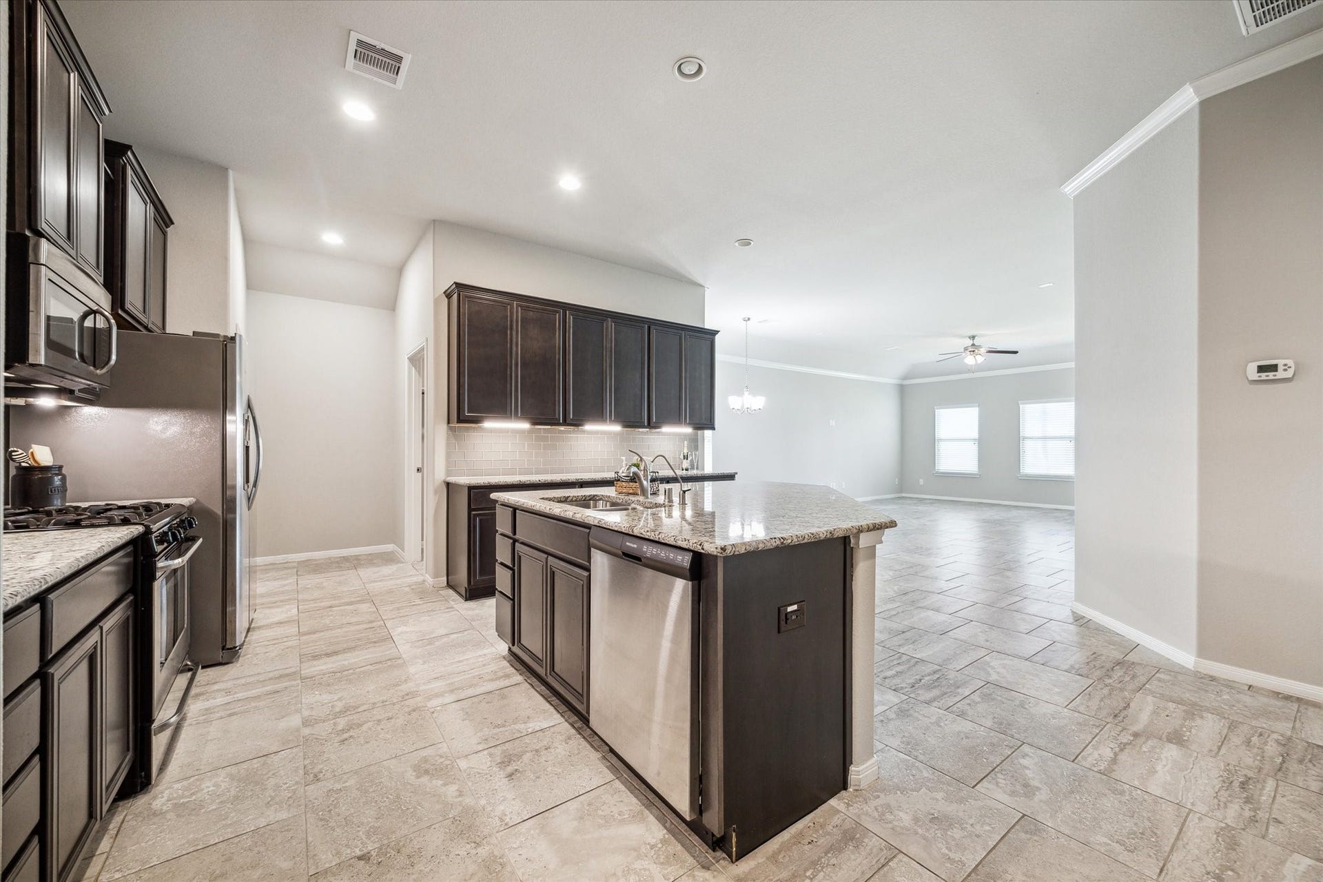 6610 Auburn Terrace Lane, Rosenberg, TX 77471 This is a modern, open-concept kitchen with dark cabinetry, stainless steel appliances, and a central island. The kitchen features granite countertops and tile flooring, and it opens up to a spacious, well-lit living area with large windows. It includes stainess steel refrigerator /freezer.