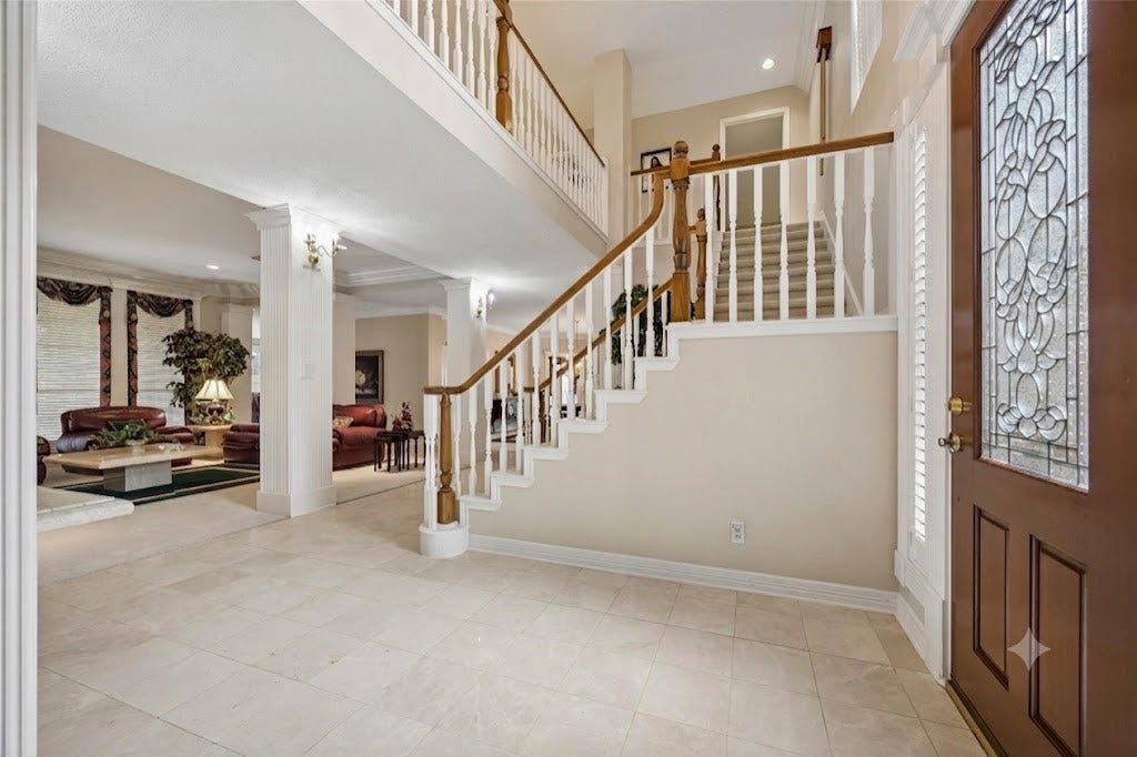 Elegant entryway featuring a grand staircase with decorative railing, leading to a spacious living area with large windows and classic finishes.