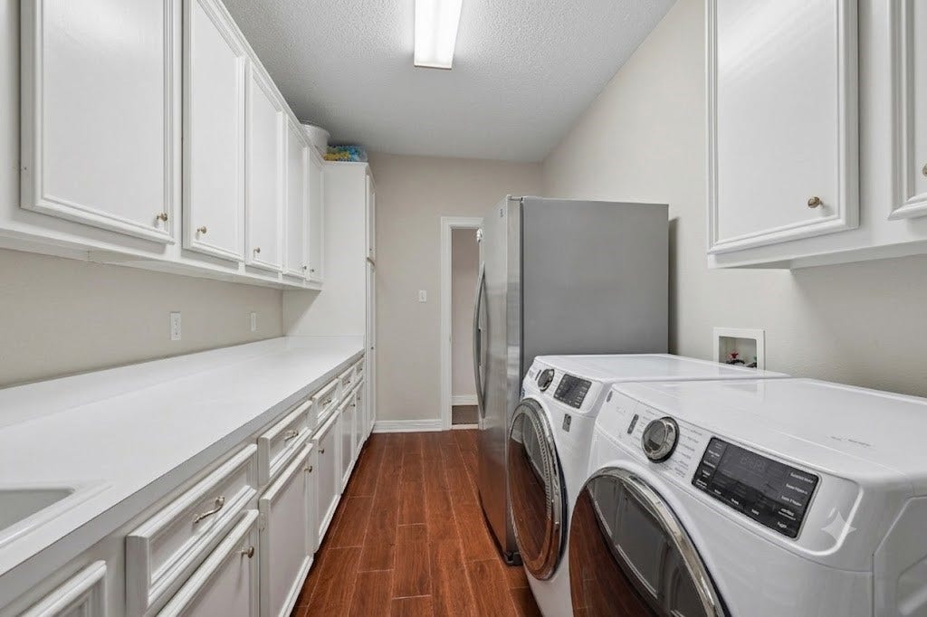 Spacious laundry room featuring sleek front-loading washer and dryer, ample cabinetry for storage, and elegant wood flooring for a clean, functional space.
