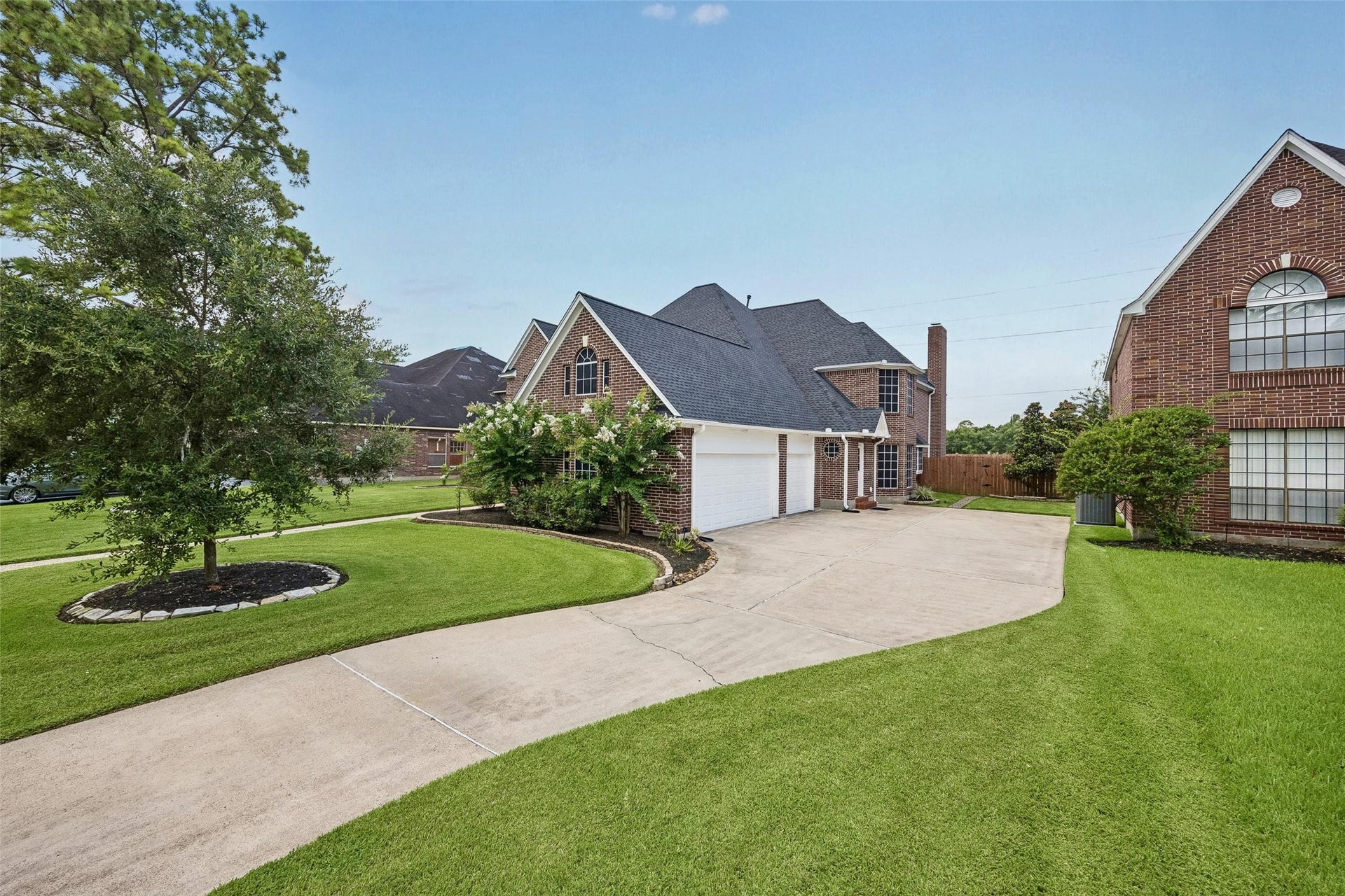 Charming brick home with a spacious driveway, a three car garage, lush green lawn, and mature trees, offering great curb appeal in a serene neighborhood setting.