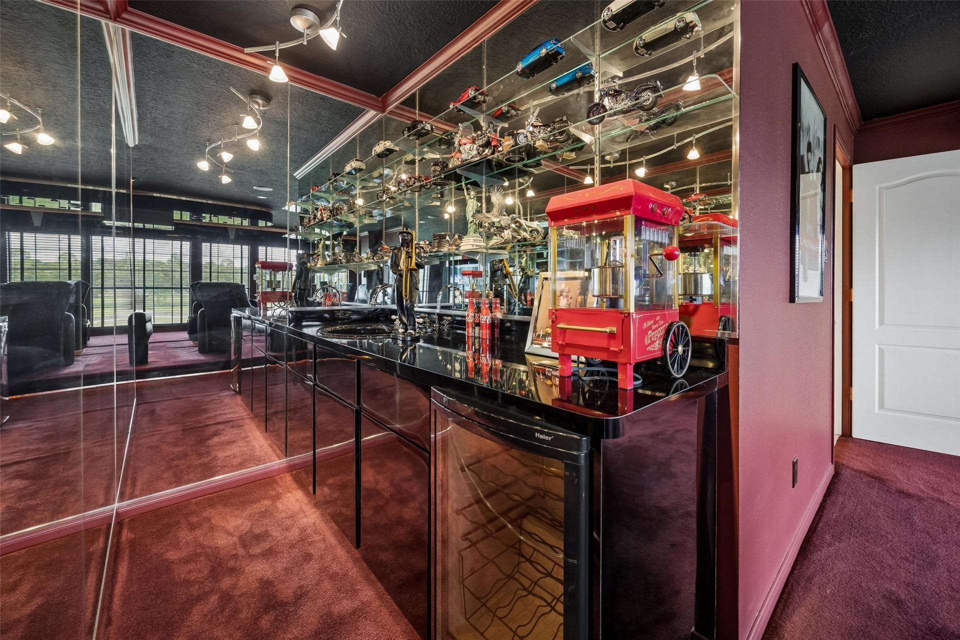 Luxurious home theater room featuring plush seating, mirrored walls, and a stylish bar area with refrigerator, a vintage popcorn machine, perfect for entertainment and relaxation. All this stays with the home.