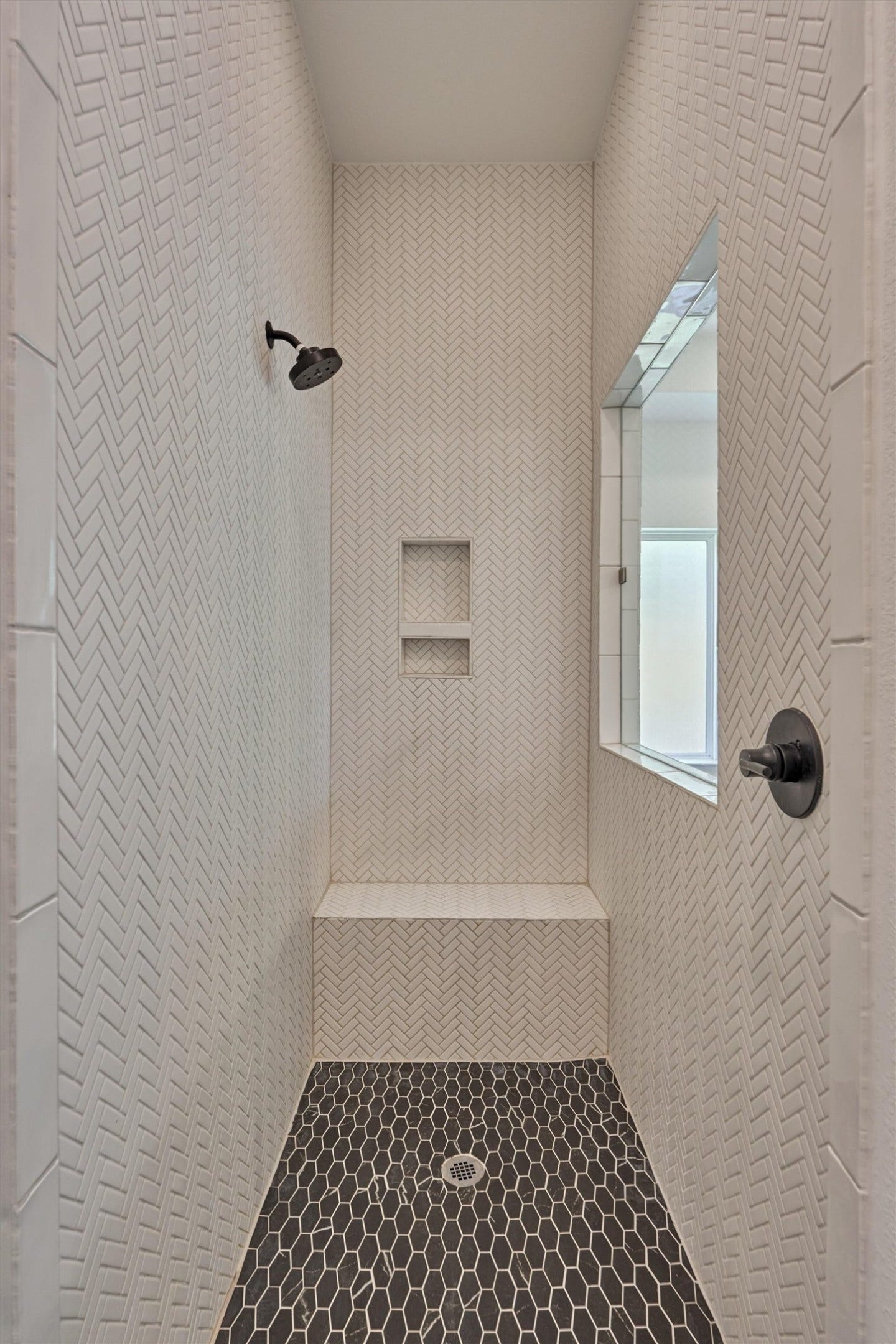 205 Patina Sorrel Drive, Montgomery, TX 77316 Elegant shower with chevron-patterned tile walls, built-in bench, and beautiful fixtures, offering a modern and refined bathing experience.