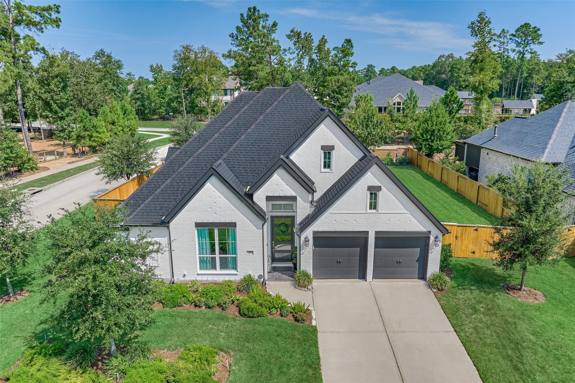 205 Patina Sorrel Drive, Montgomery, TX 77316 Charming modern home with a sleek black roof and a pristine white exterior, featuring a double garage and lush landscaping in a serene neighborhood setting.