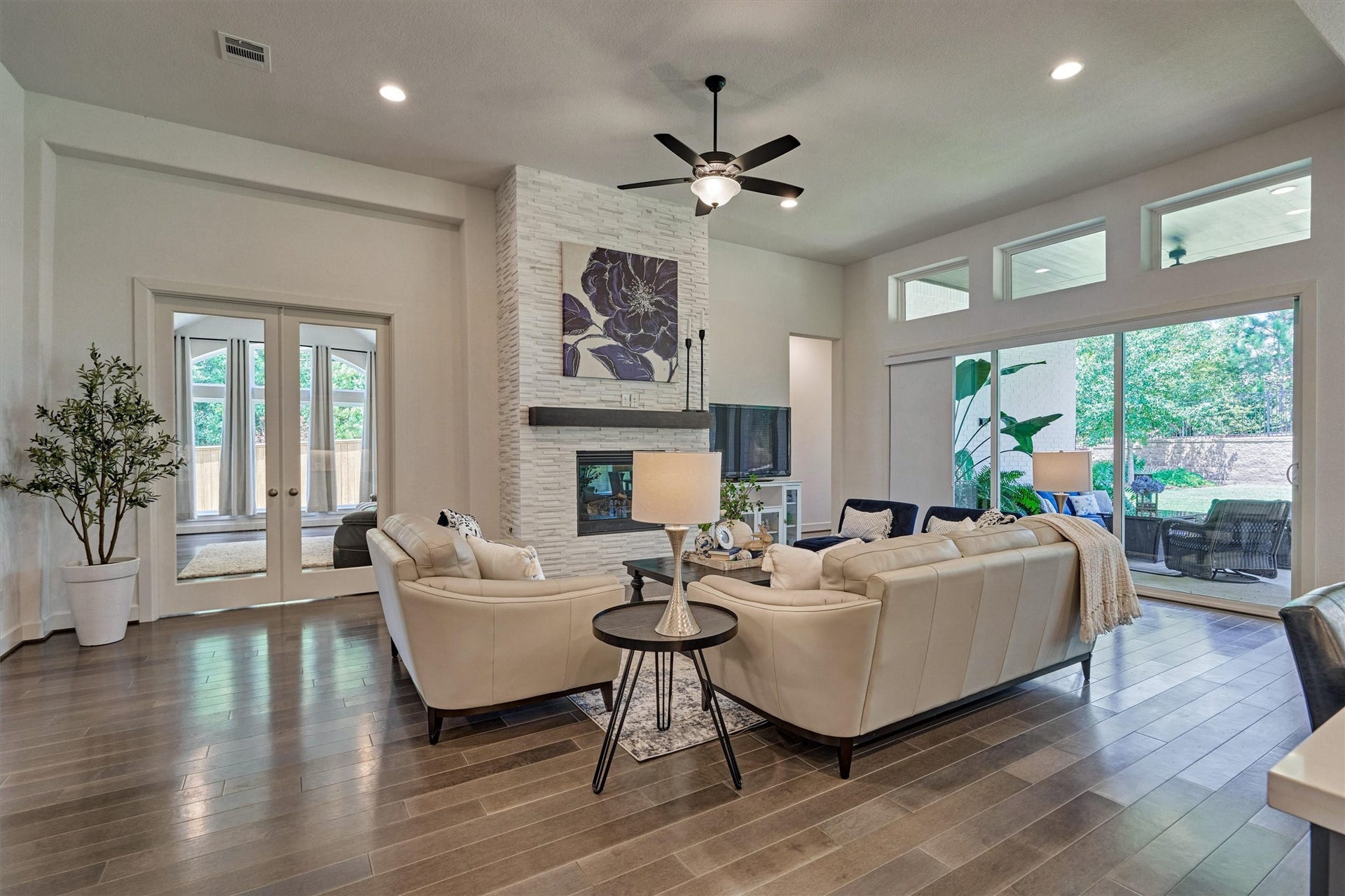 205 Patina Sorrel Drive, Montgomery, TX 77316 Spacious living room with elegant wood flooring, a modern stone fireplace, and abundant natural light from large windows and sliding glass doors, leading to a serene outdoor patio.