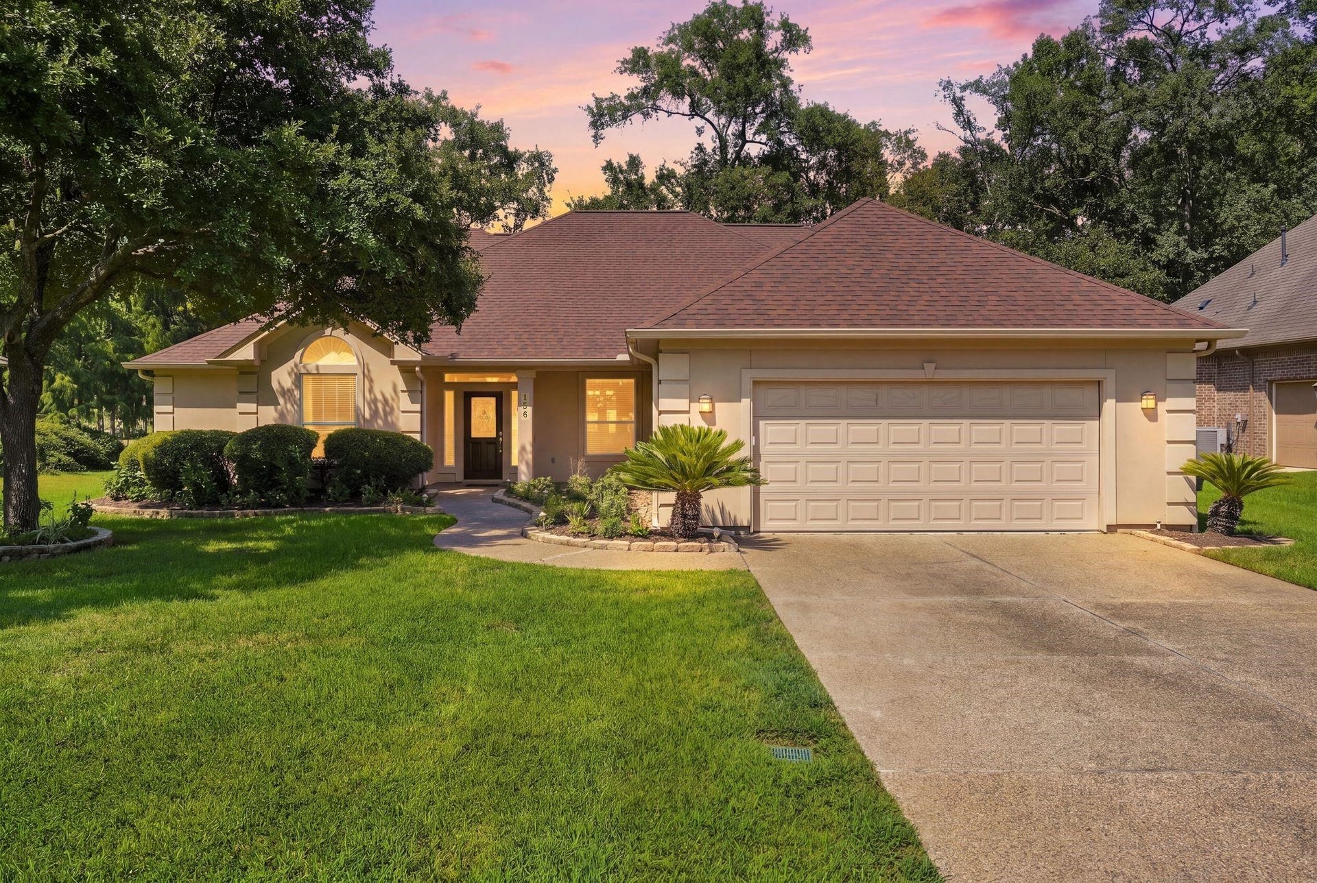 156 April Waters Drive W, Conroe, TX 77356 Charming single-story home with a spacious two-car garage, surrounded by lush greenery and mature trees.