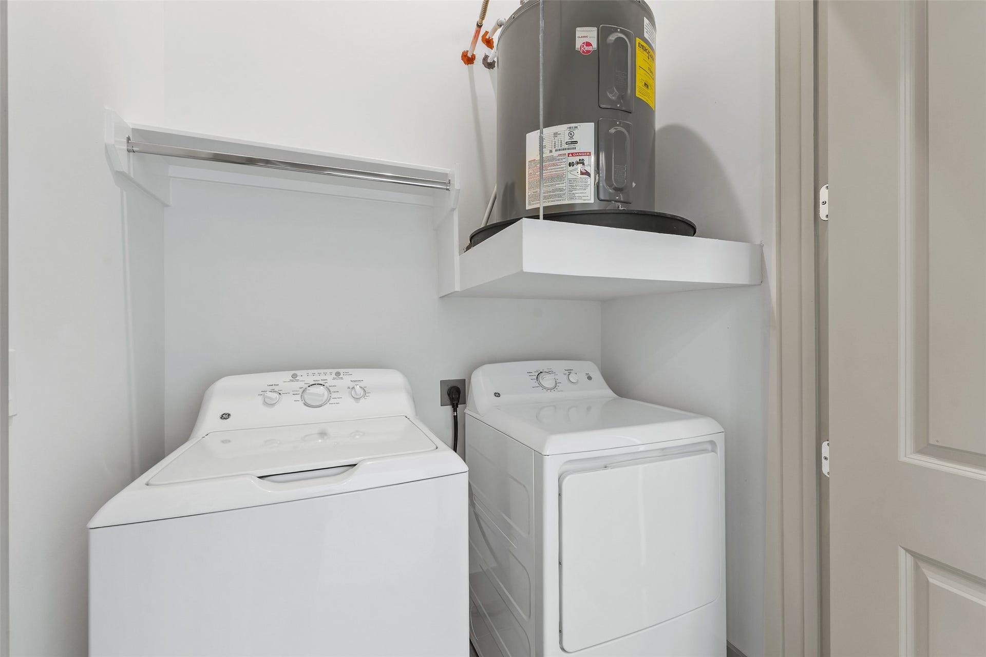 170 Malone Street, #3402, Houston, TX 77007 This photo shows a compact laundry area with a washer and dryer side by side, a shelf above the dryer, and a water heater mounted on a platform. The space is clean, functional, and efficiently organized.