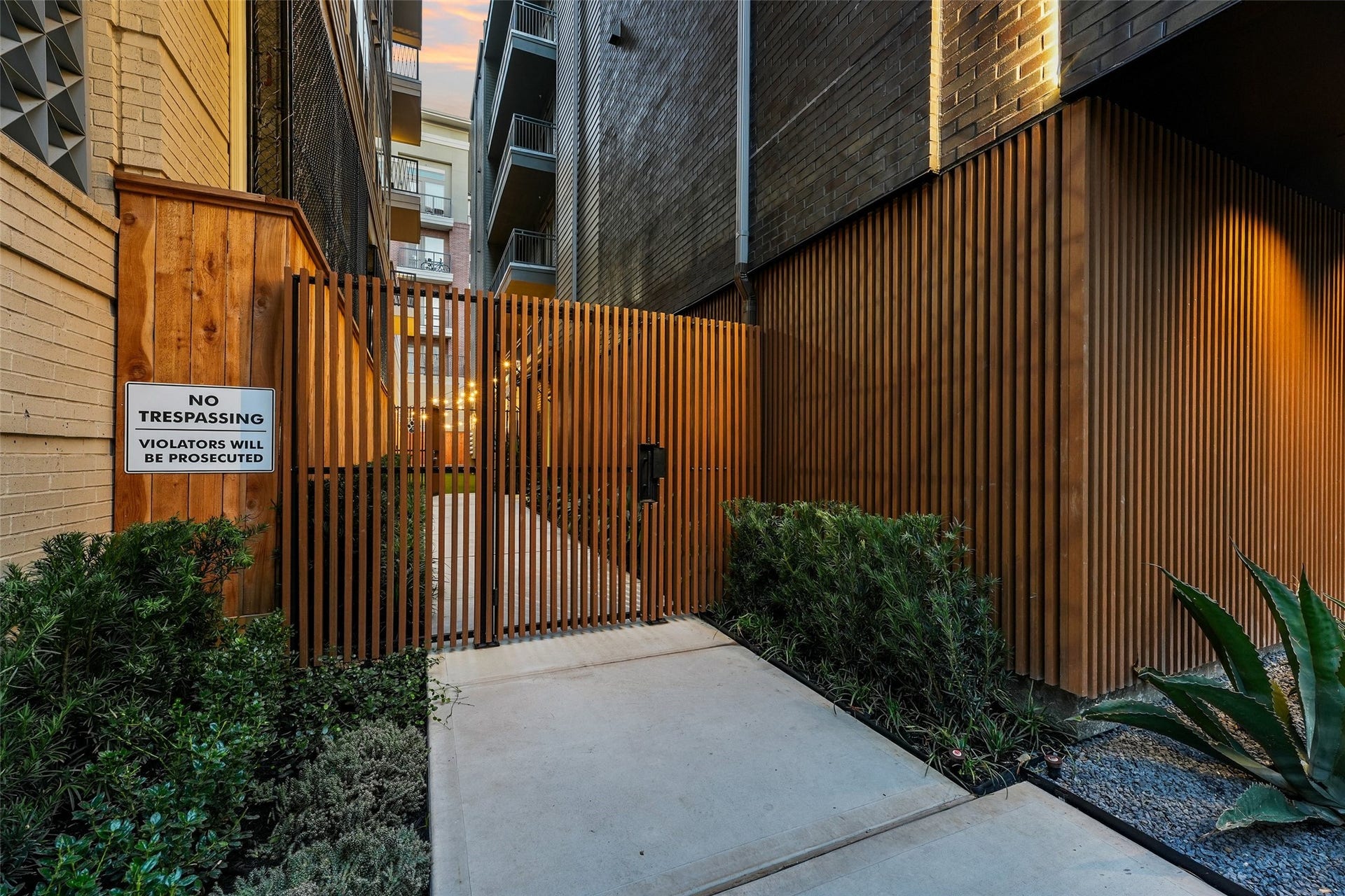170 Malone Street, #3402, Houston, TX 77007 This photo features a modern, secure entrance with a wooden slat gate, surrounded by contemporary brick and wood walls. The area is landscaped with low-maintenance plants, offering a private and stylish entryway.