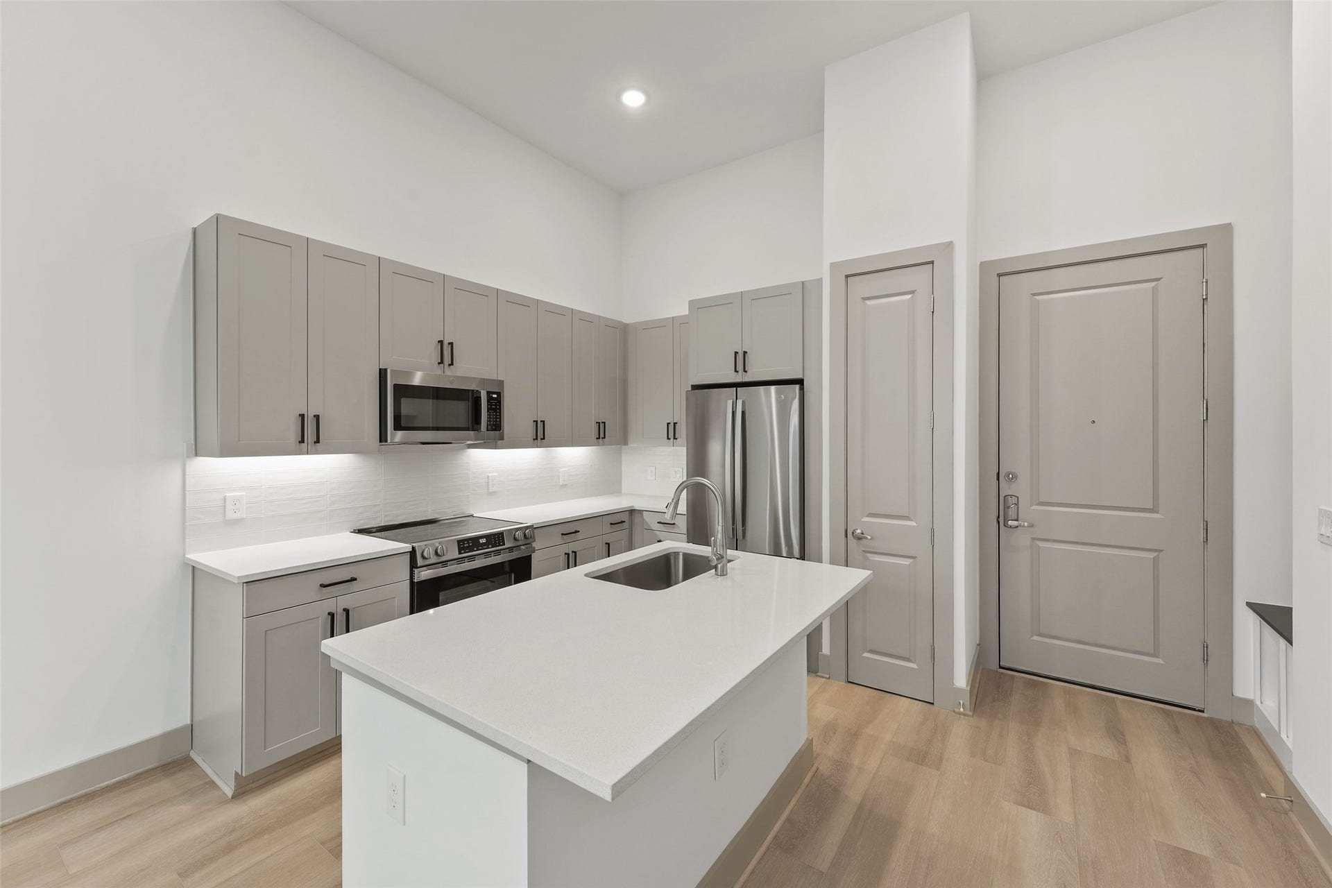 170 Malone Street, #3402, Houston, TX 77007 This modern kitchen features sleek gray cabinetry, stainless steel appliances, and a spacious island with a sink. The light wood flooring complements the clean, white countertops and backsplash, creating a bright and inviting space.