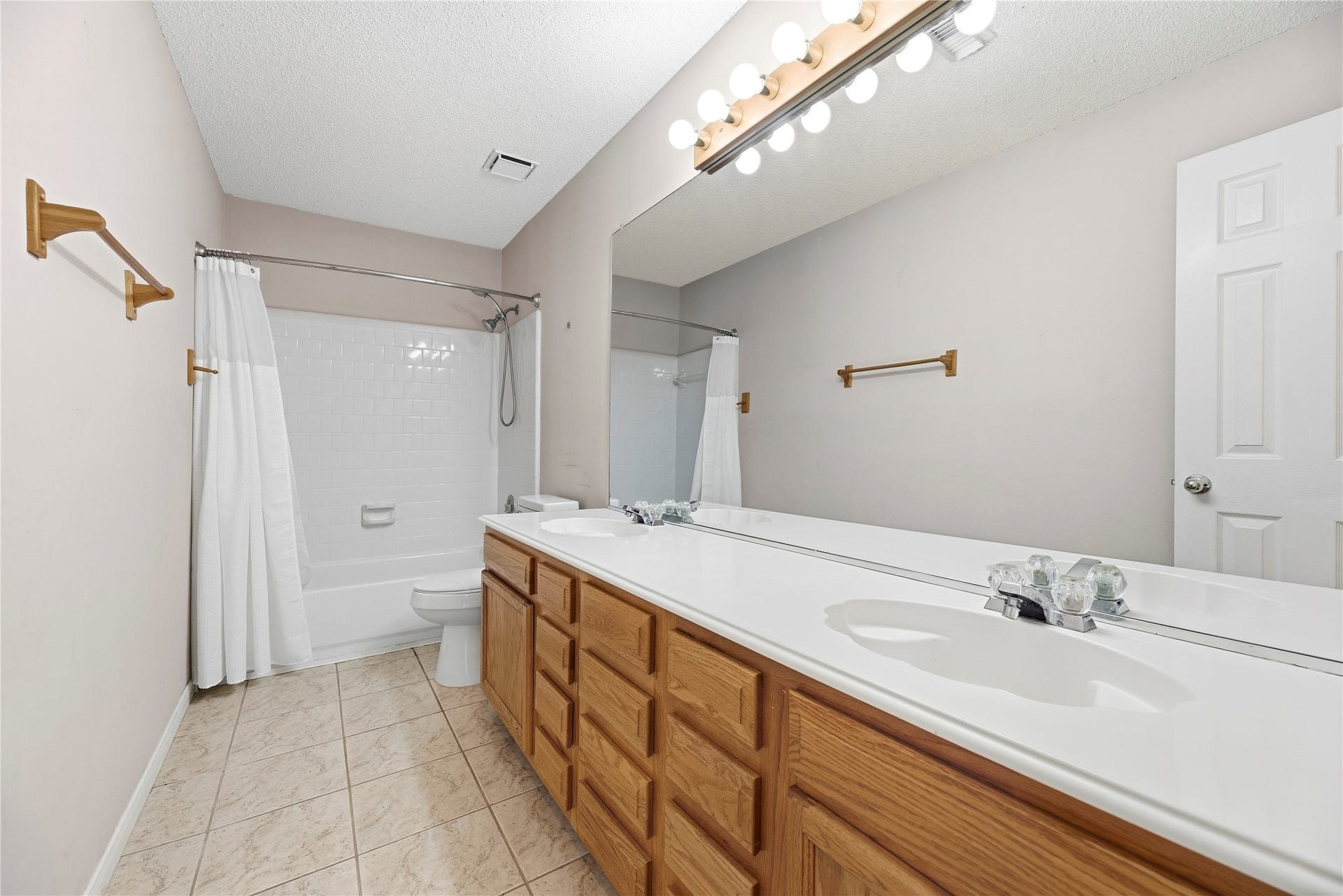 9922 W Cedaredge Drive, Houston, TX 77064 Spacious secondary bathroom #1 featuring dual sinks, a large mirror, tiled flooring, and a shower-tub combo with a sleek white curtain.