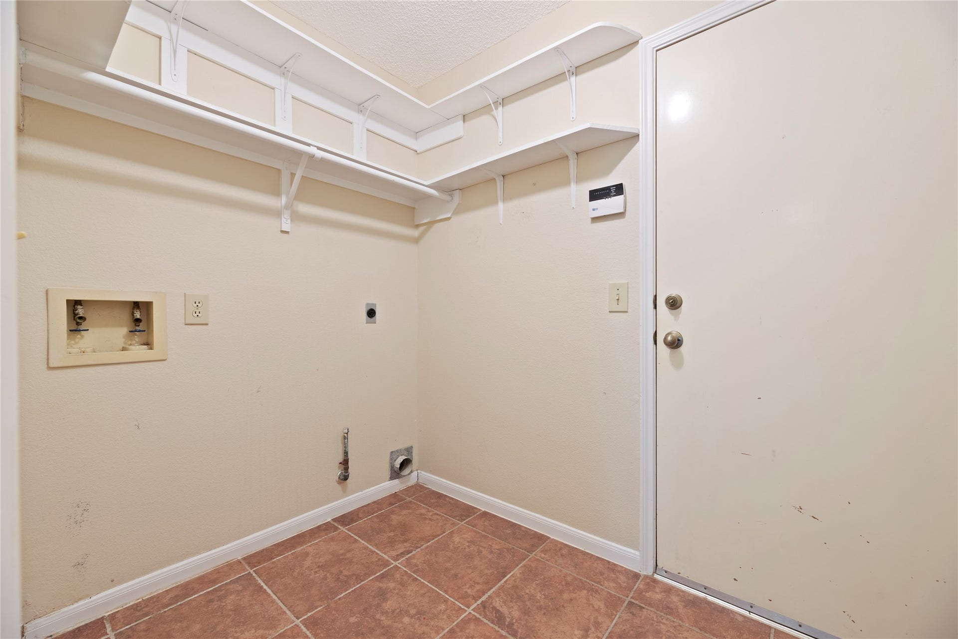 9922 W Cedaredge Drive, Houston, TX 77064 Spacious laundry room features tiled flooring, wall-mounted shelves for storage, and hookups for washer and dryer, offering convenience and functionality.