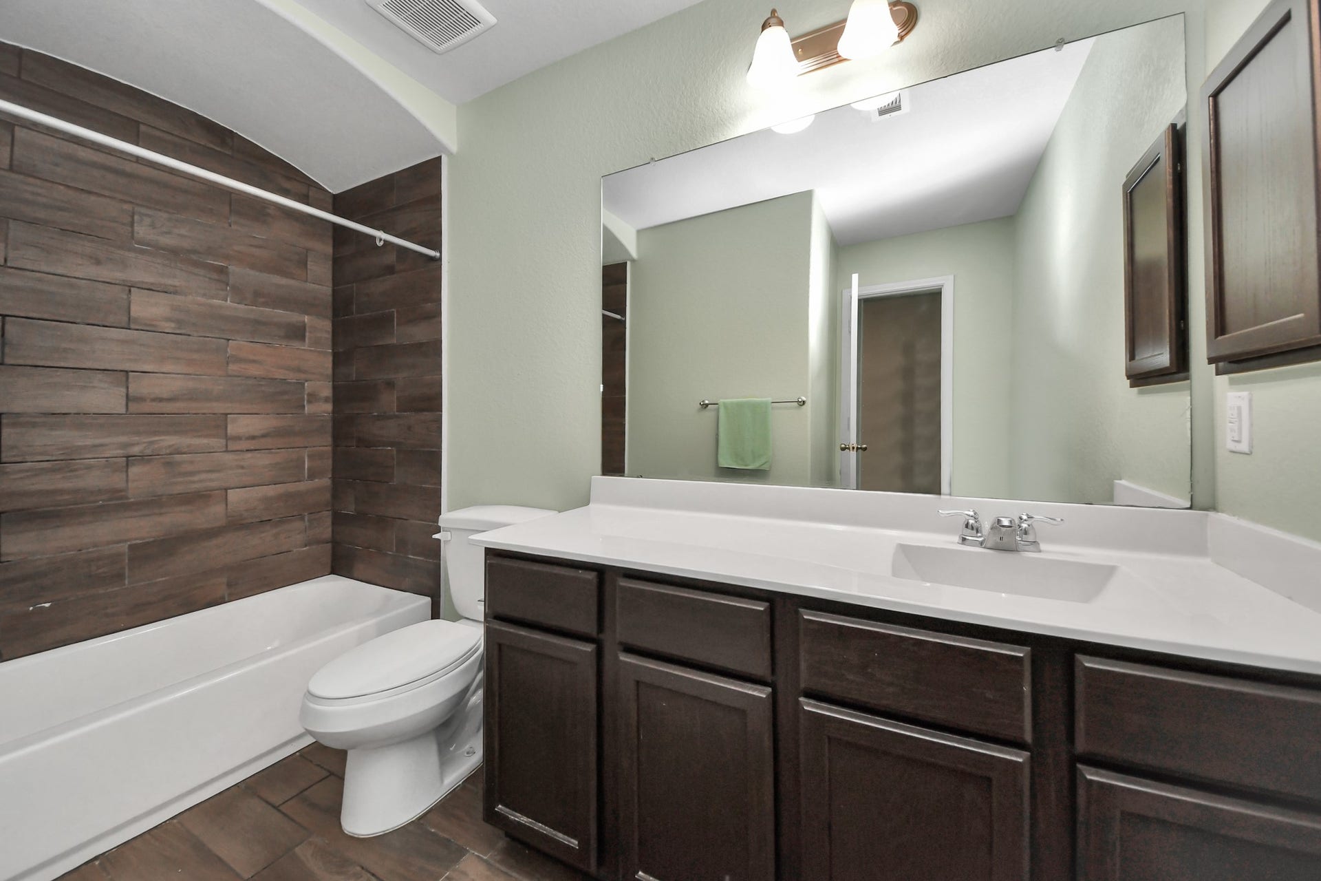 Upstairs secondary full bathroom features a tub-and-shower combination with wood-look tile, a spacious vanity and ample cabinet storage.
