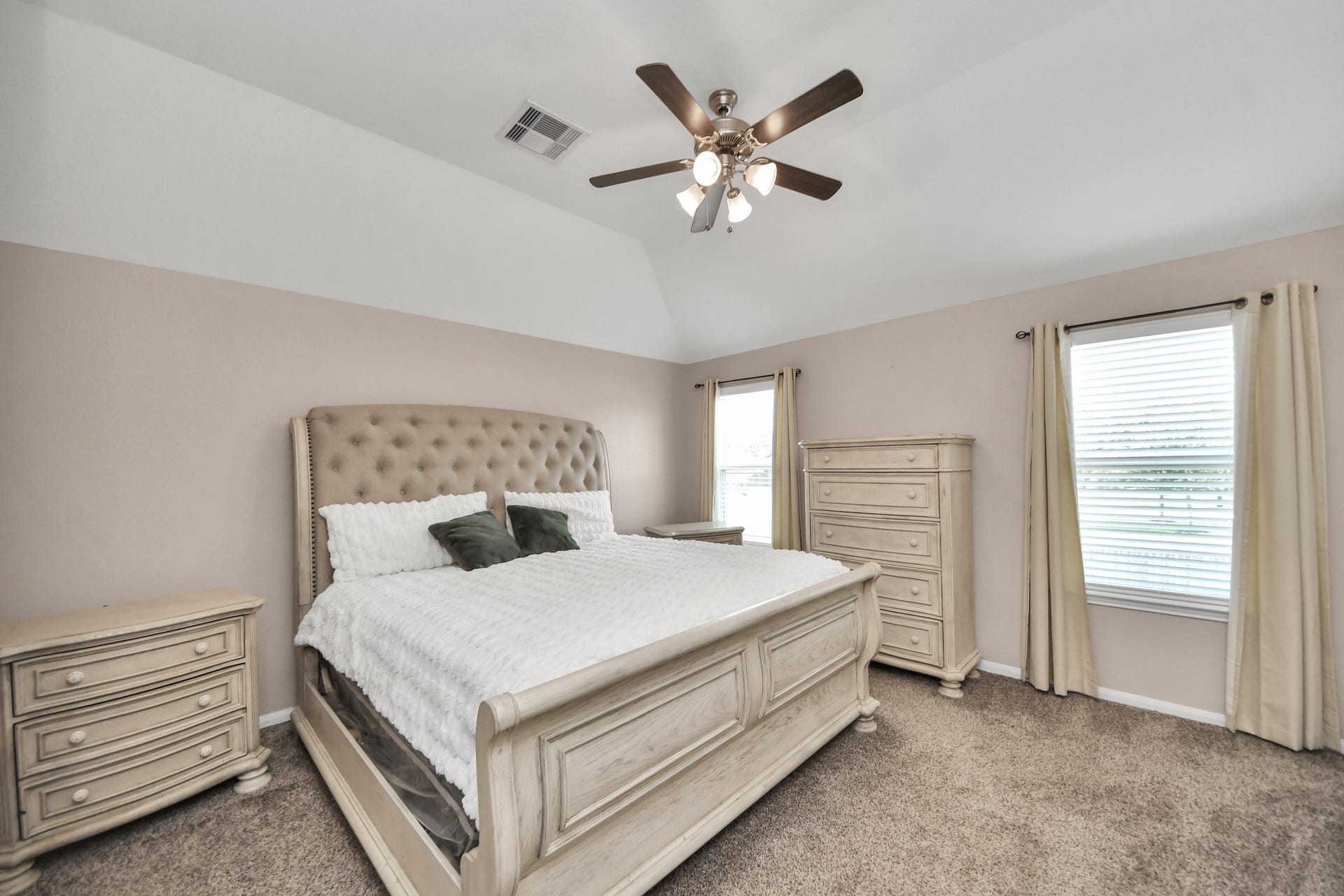 Expansive primary bedroom features high tray ceilings and multiple windows that fill the space with natural light.