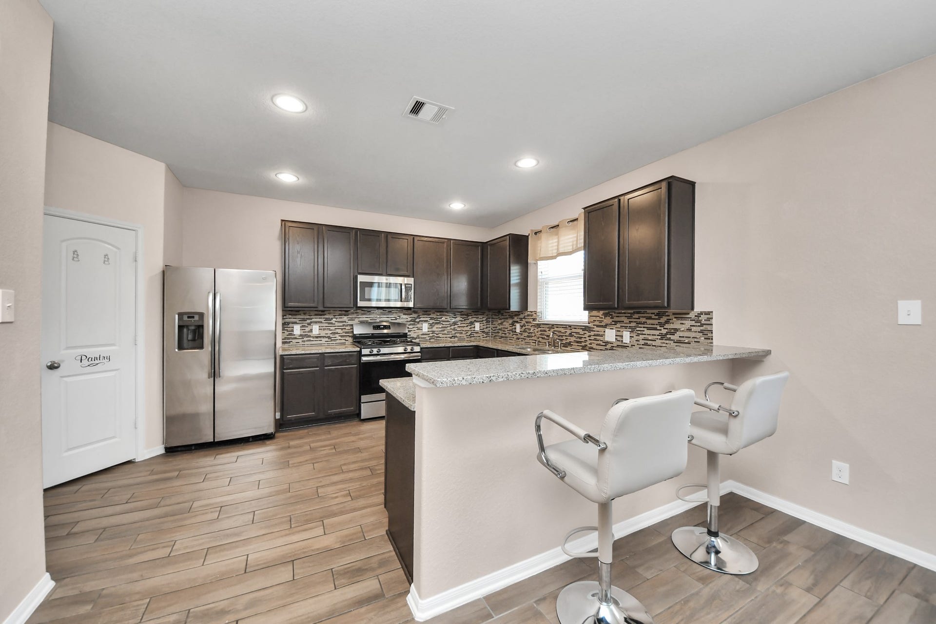 Spacious kitchen featuring granite countertops, stainless-steel appliances, abundant cabinetry, a walk-in pantry and breakfast bar seating.