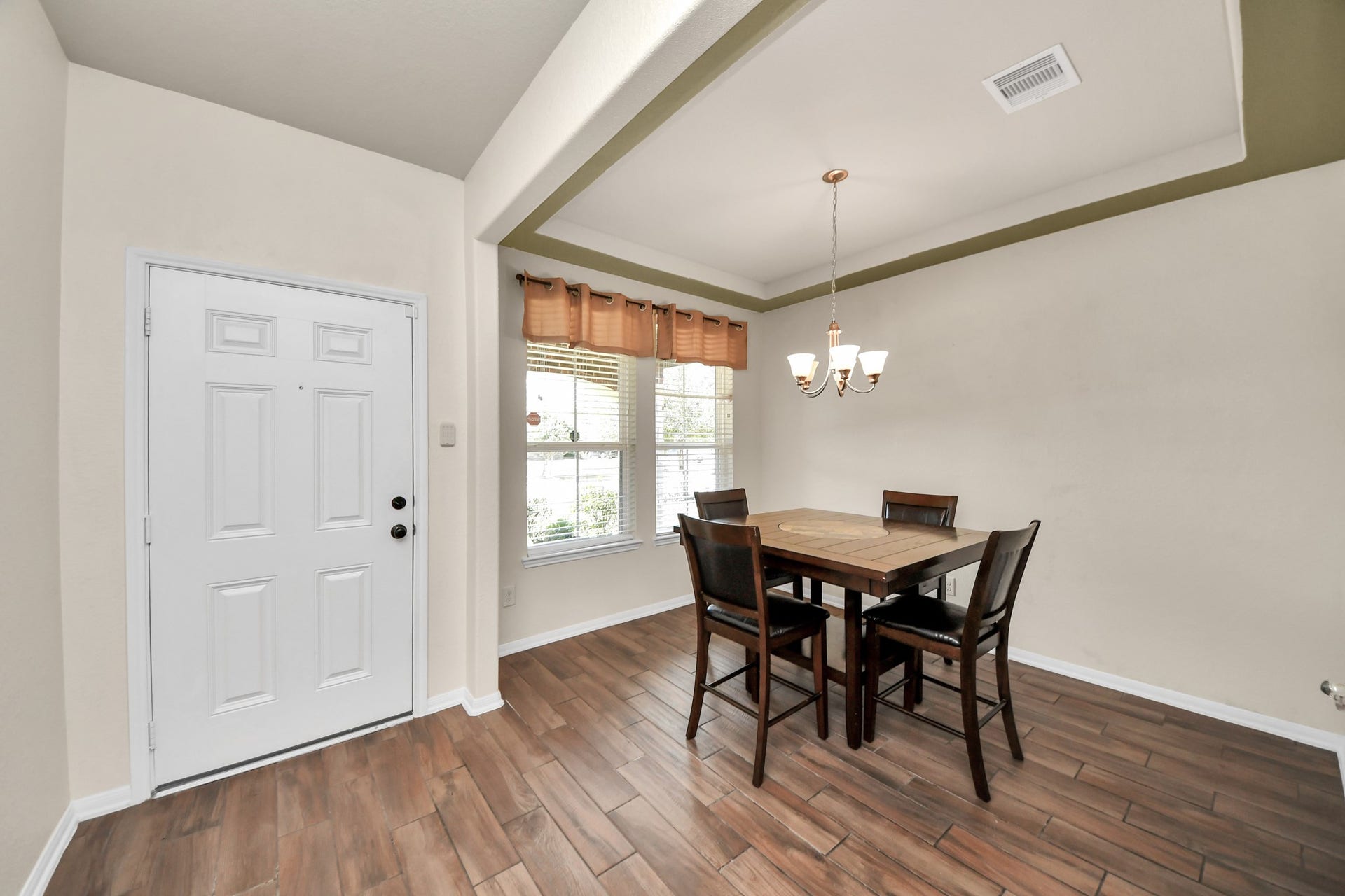 Bright dining area featuring a tray ceiling, chandelier, large windows and wood-look tile flooring.