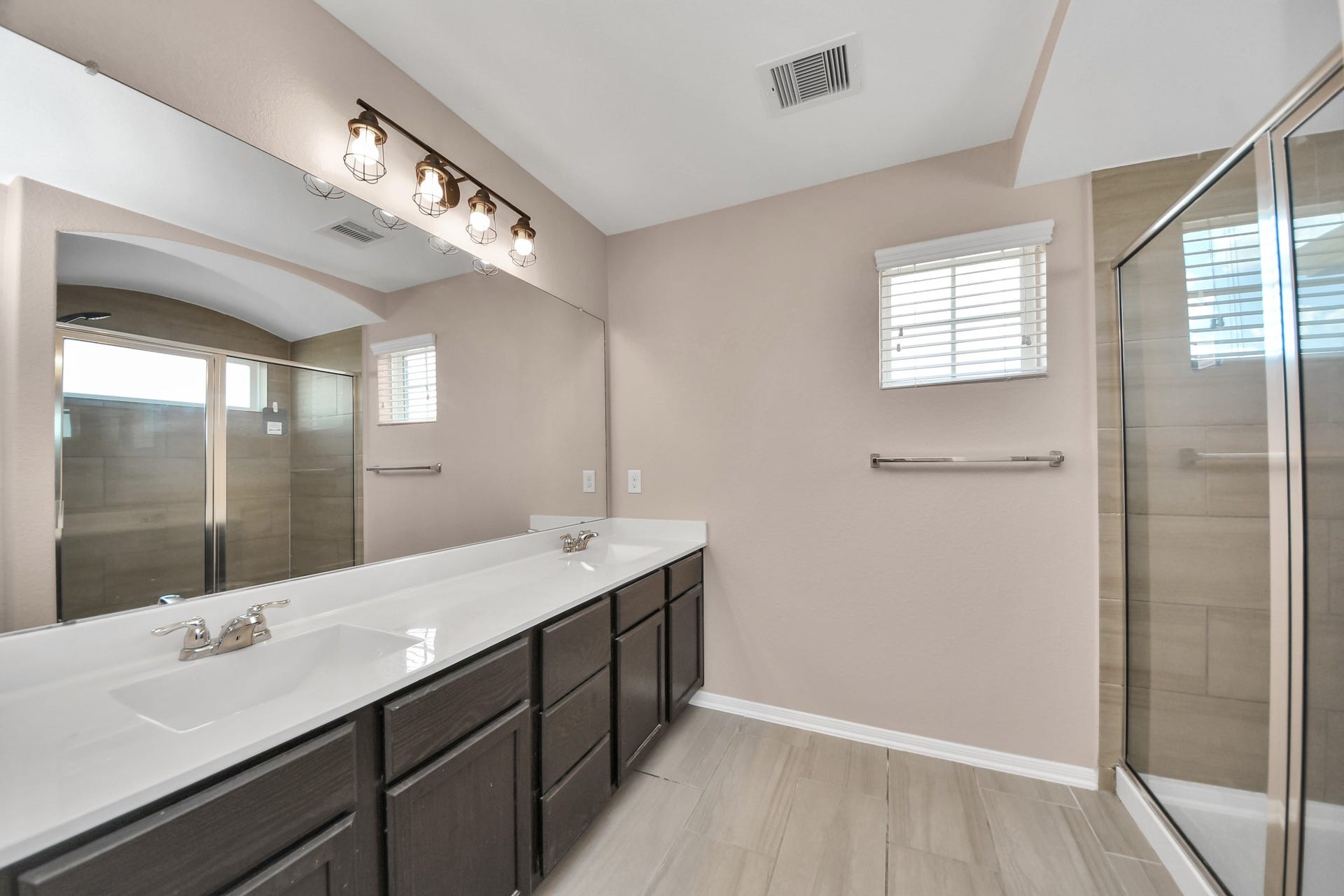 Spacious primary bathroom features a dual-sink vanity, oversized mirror, abundant cabinetry and a glass-enclosed shower.
