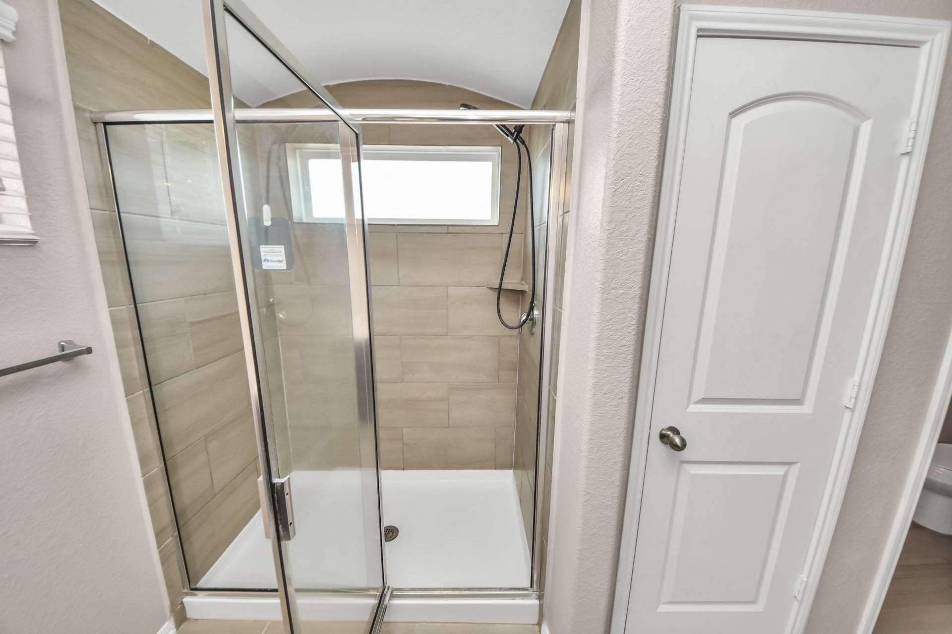 Tiled walk-in shower features a handheld showerhead and natural light, with a convenient linen closet located to the right.