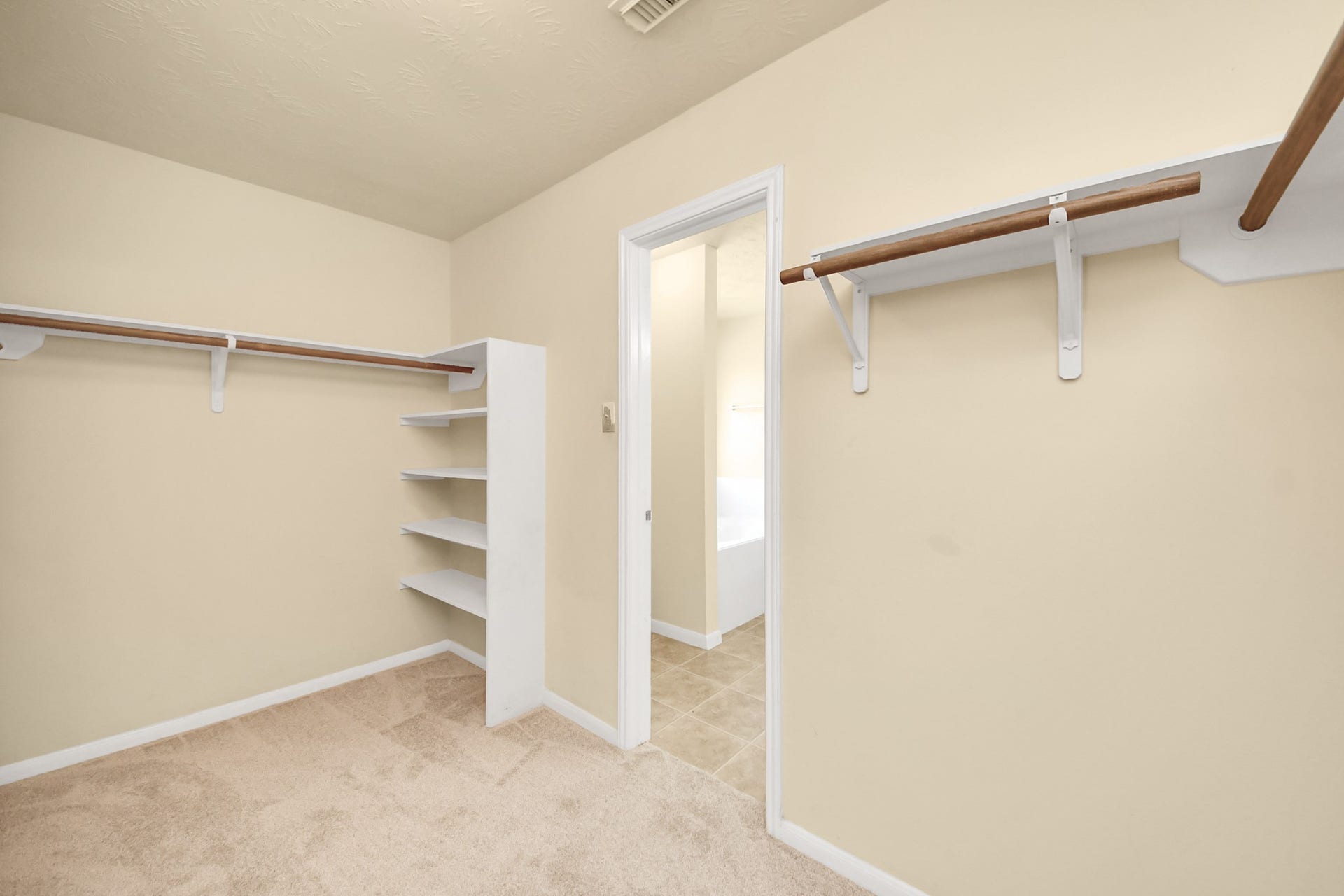 Spacious walk-in closet with ample shelving and hanging space, connected to a tiled bathroom for convenience.