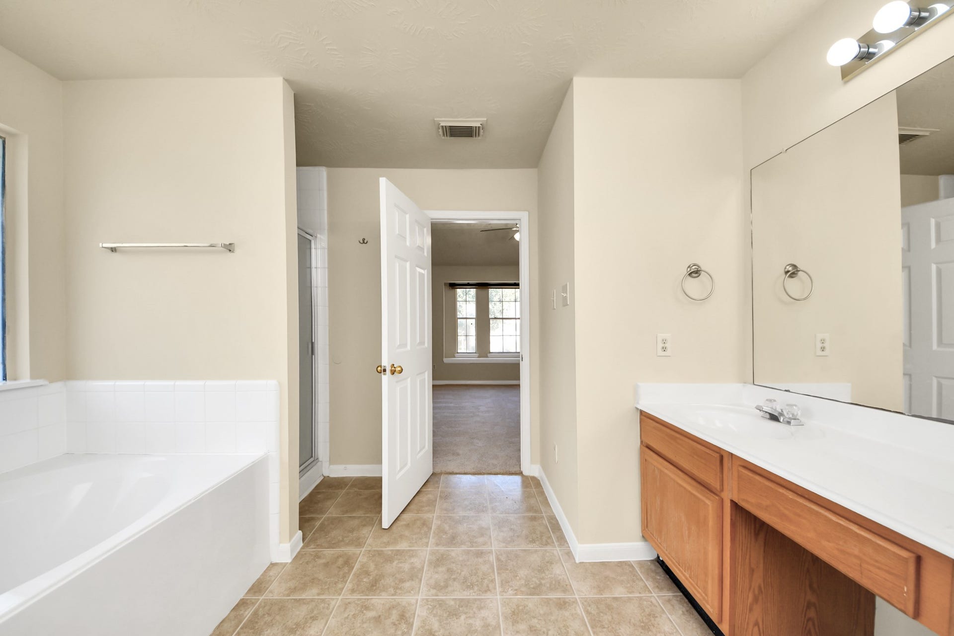 Spacious bathroom featuring a large soaking tub, dual-sink vanity, tile flooring, and large closet.