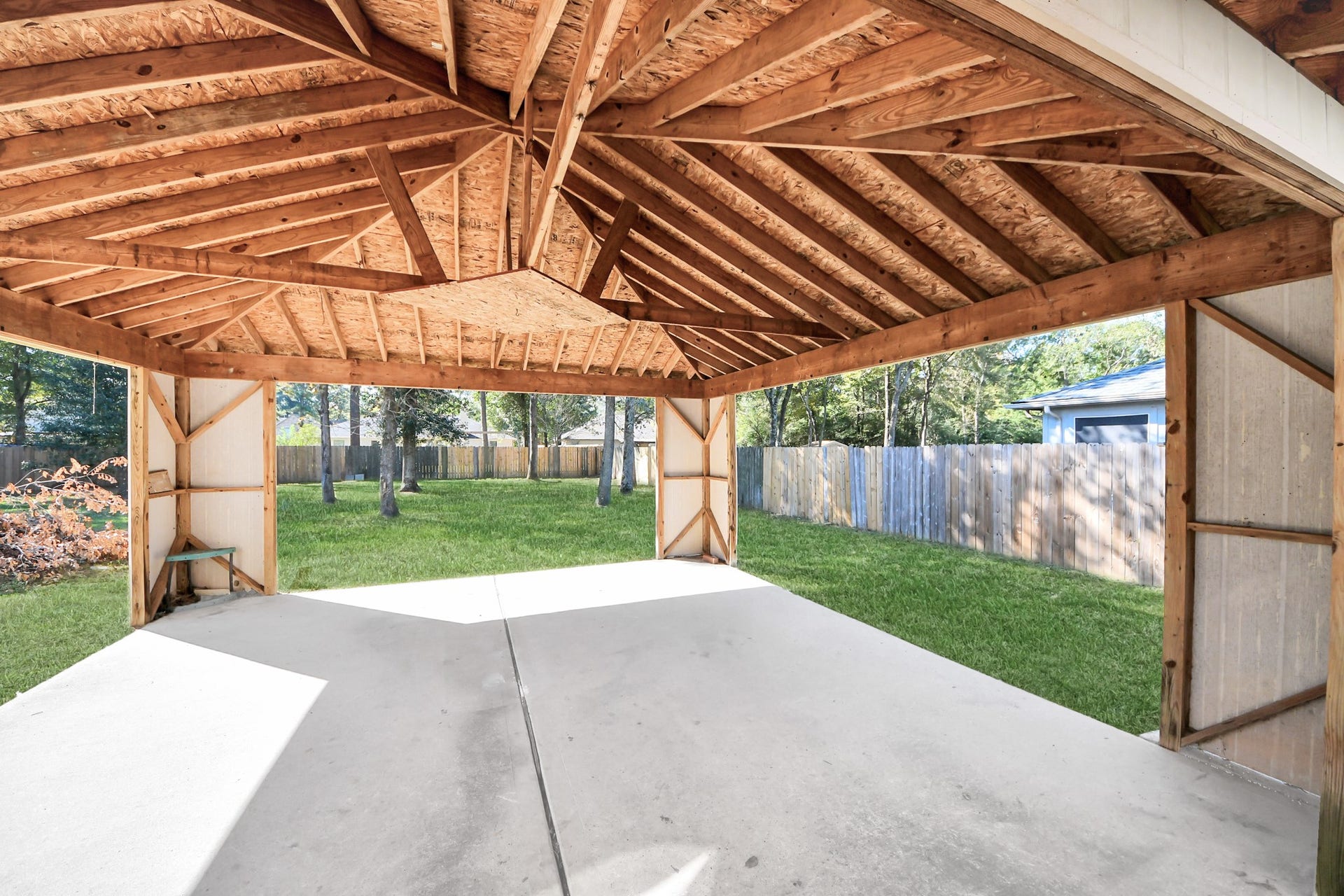 Huge covered patio with a sturdy wooden ceiling, offering a great view of the backyard, ideal for outdoor gatherings and relaxation.