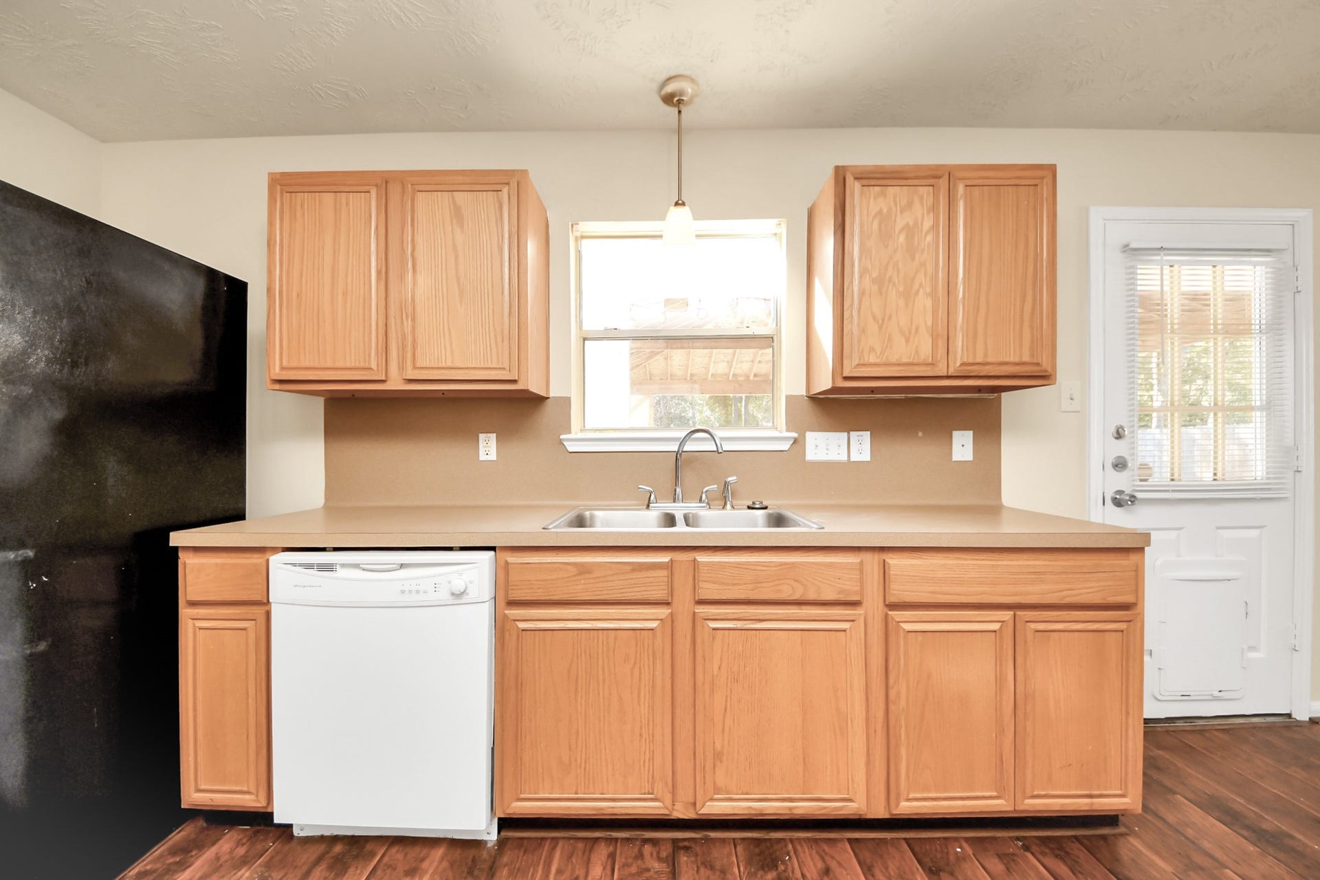 Bright kitchen with a double sink, appliances included, featuring a window and door leading to covered patio in your large backyard.