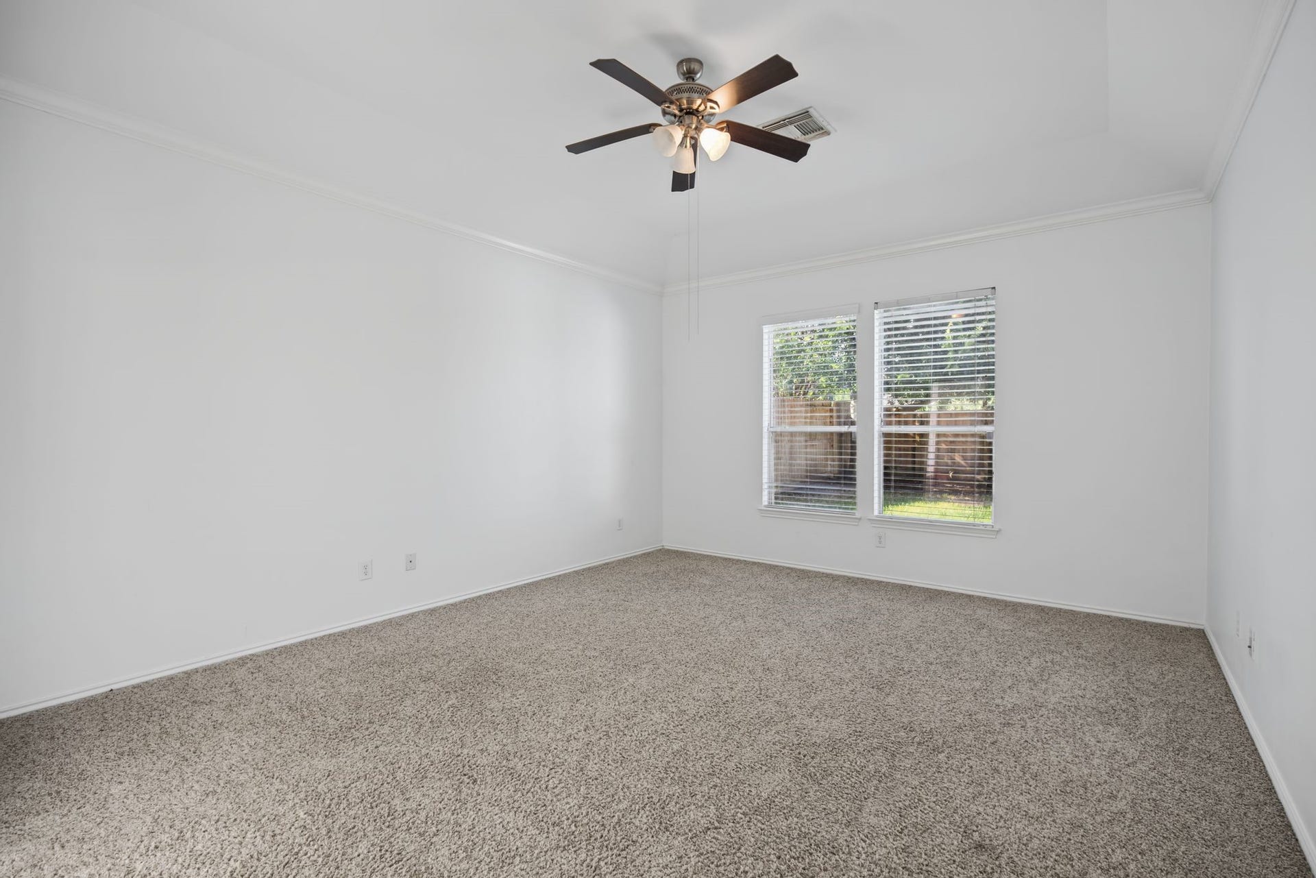 Retreat to the first-floor primary bedroom, featuring paired windows, soft carpeted flooring, and a ceiling fan with lighting.