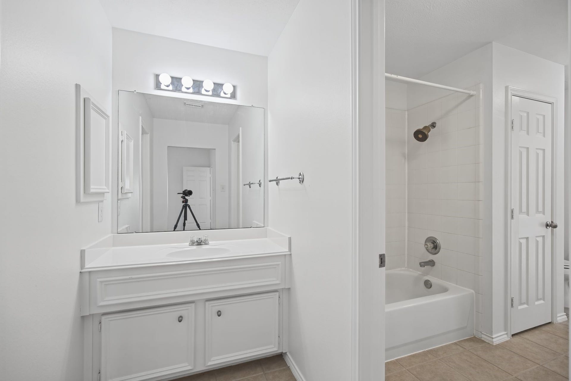 The adjoining bathroom features a white vanity, illuminated mirror, and a tub-and-shower combination.