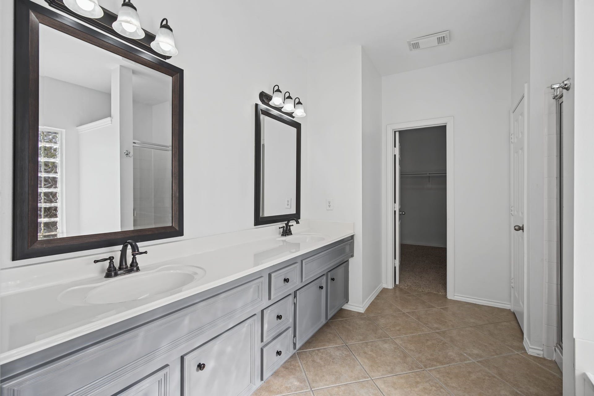 The primary bathroom offers an extended double-sink vanity, framed mirrors, and coordinating lighting for a balanced, refined presentation.